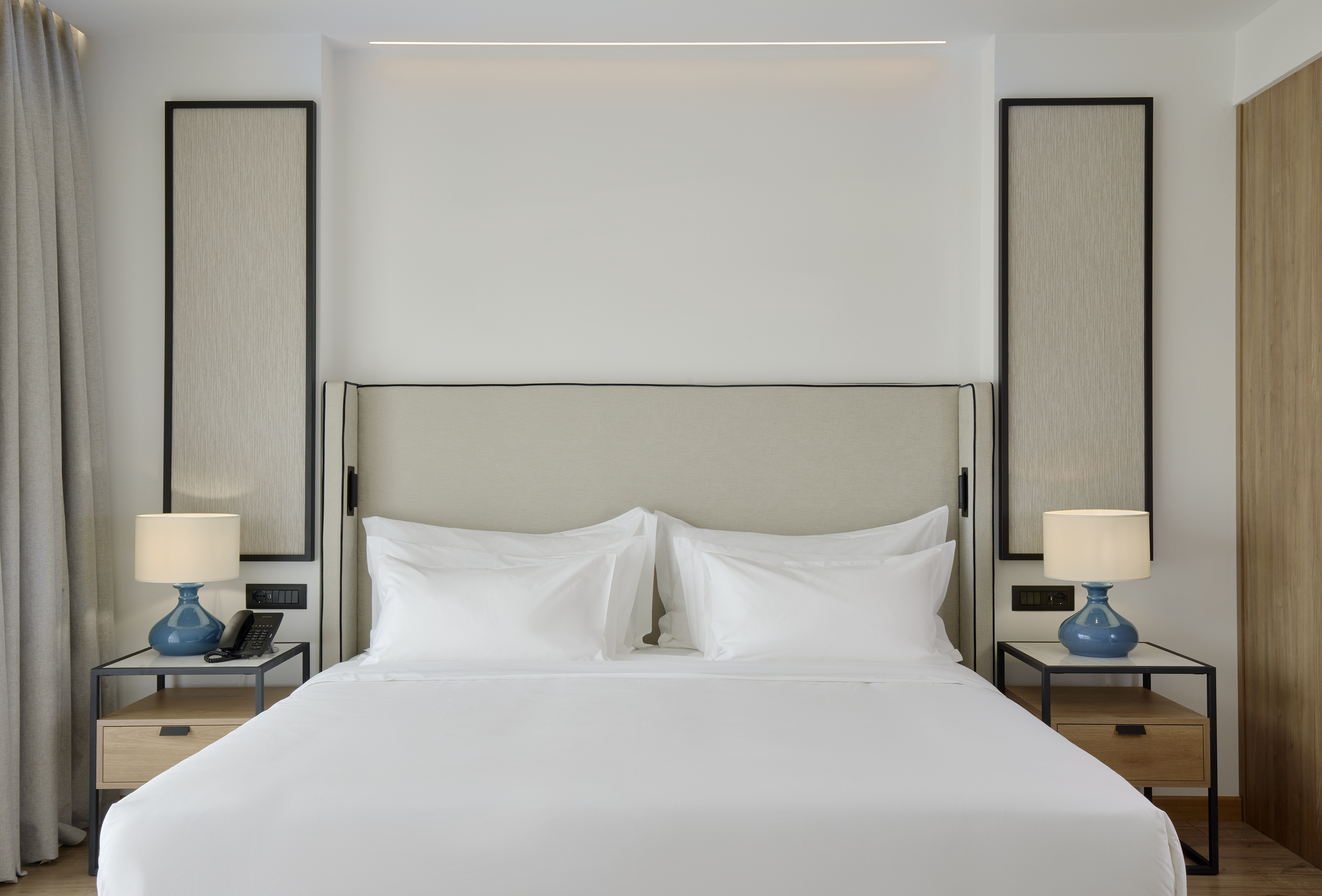 a bed with white sheets and a blue lamp on a table