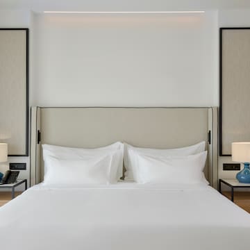 a bed with white sheets and a blue lamp on a table