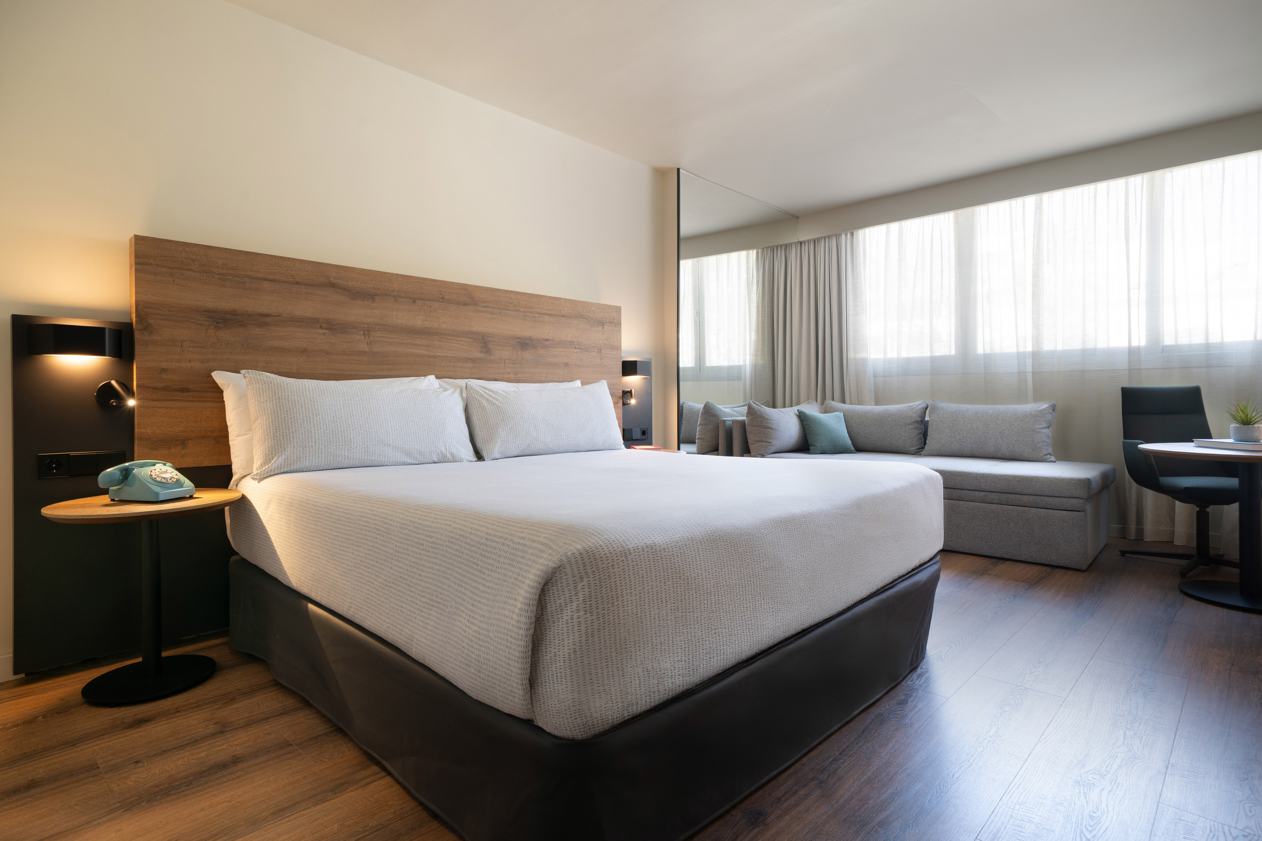 Modern hotel room with king bed, wood accents, sofa, and large windows.