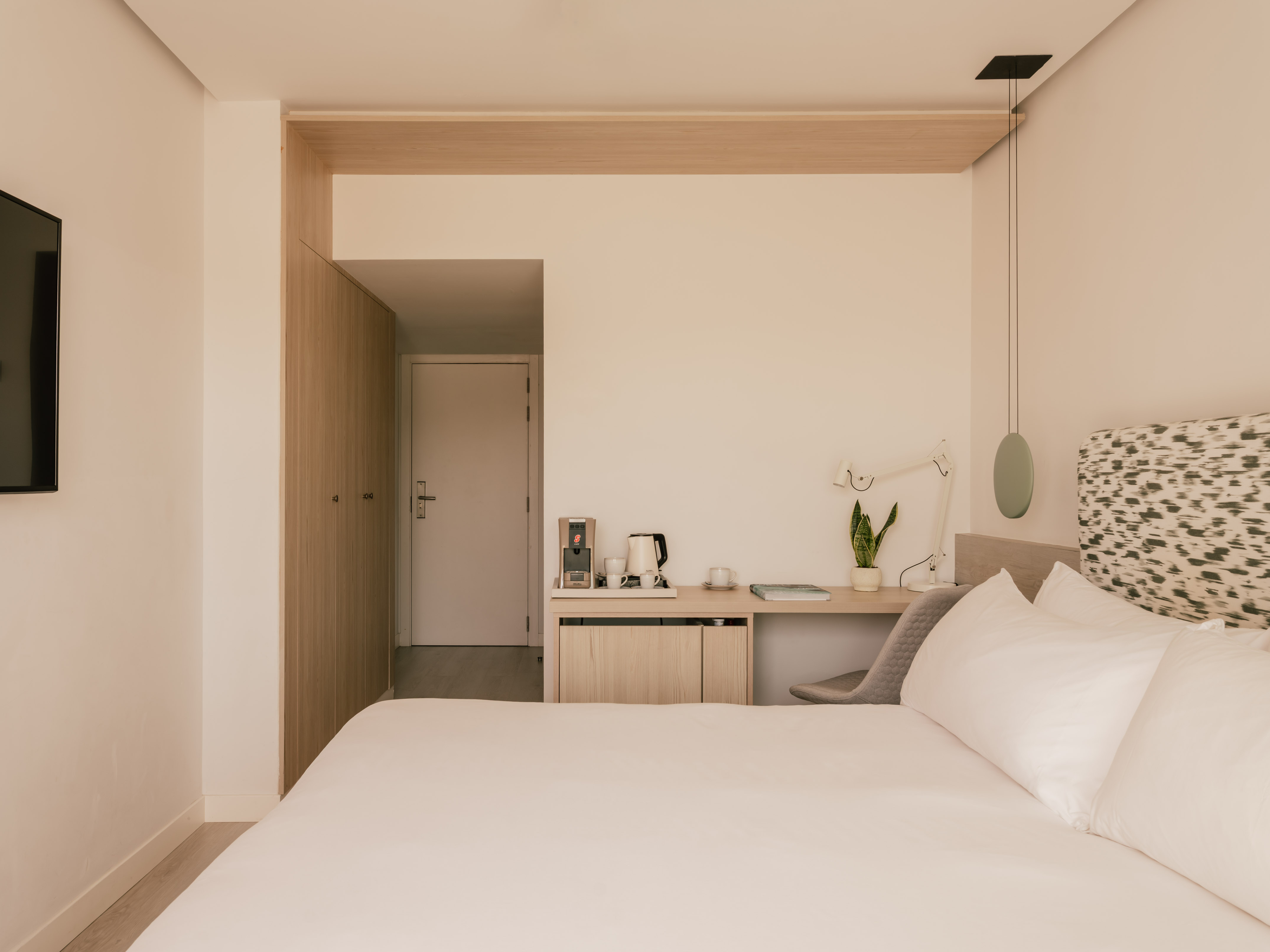 Habitación de hotel moderna con cama, escritorio, cafetera y armario de madera.