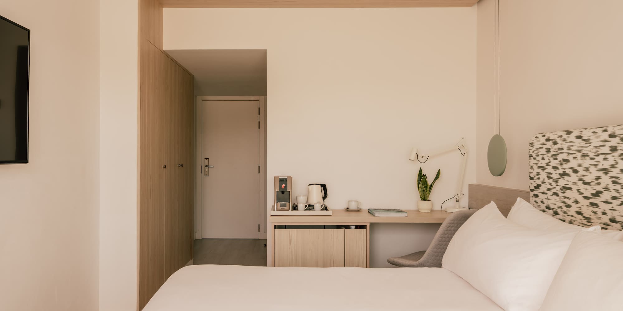 Modern hotel room with queen bed, minimalist desk, and light wood accents.