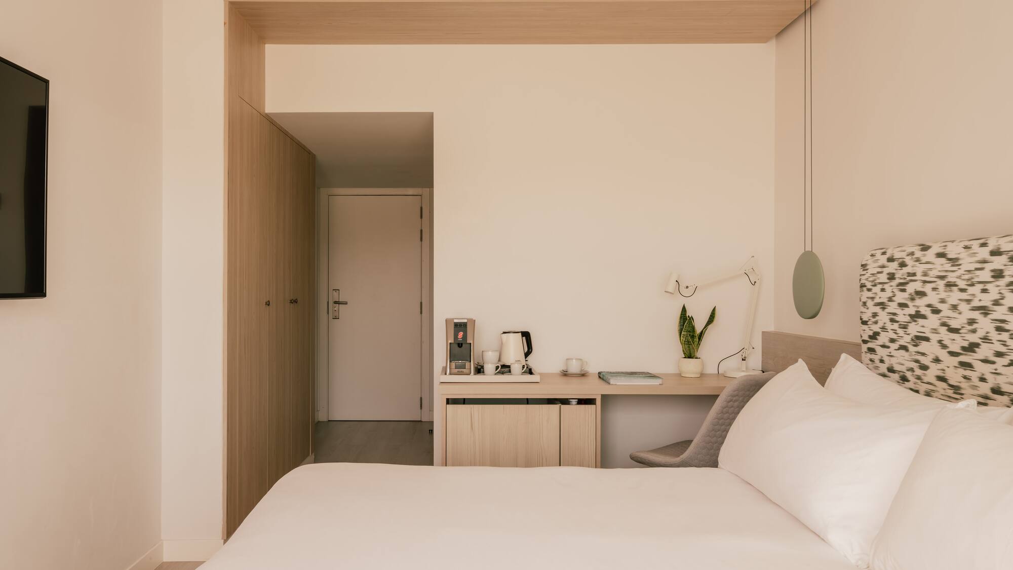 Modern hotel room with queen bed, minimalist desk, and light wood accents.