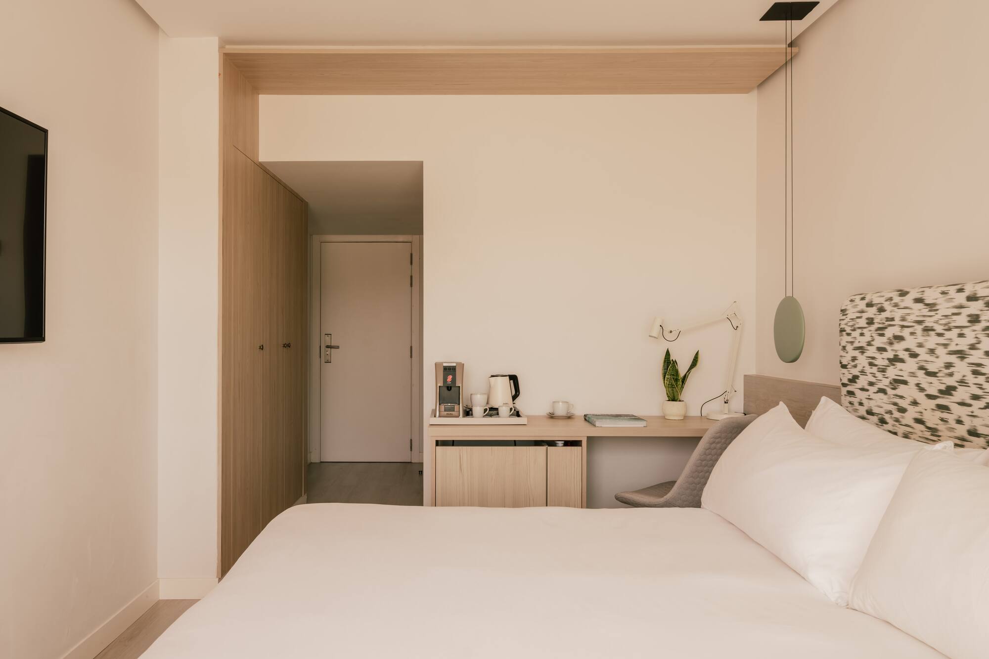 Habitación de hotel moderna con cama, escritorio, cafetera y armario de madera.