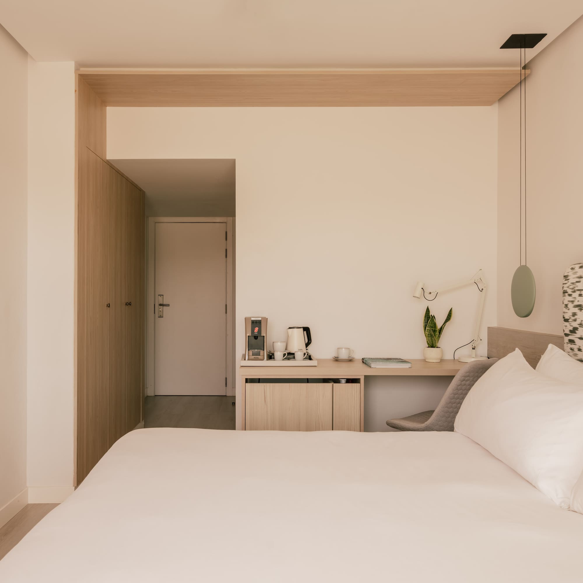 Modern hotel room with queen bed, minimalist desk, and light wood accents.