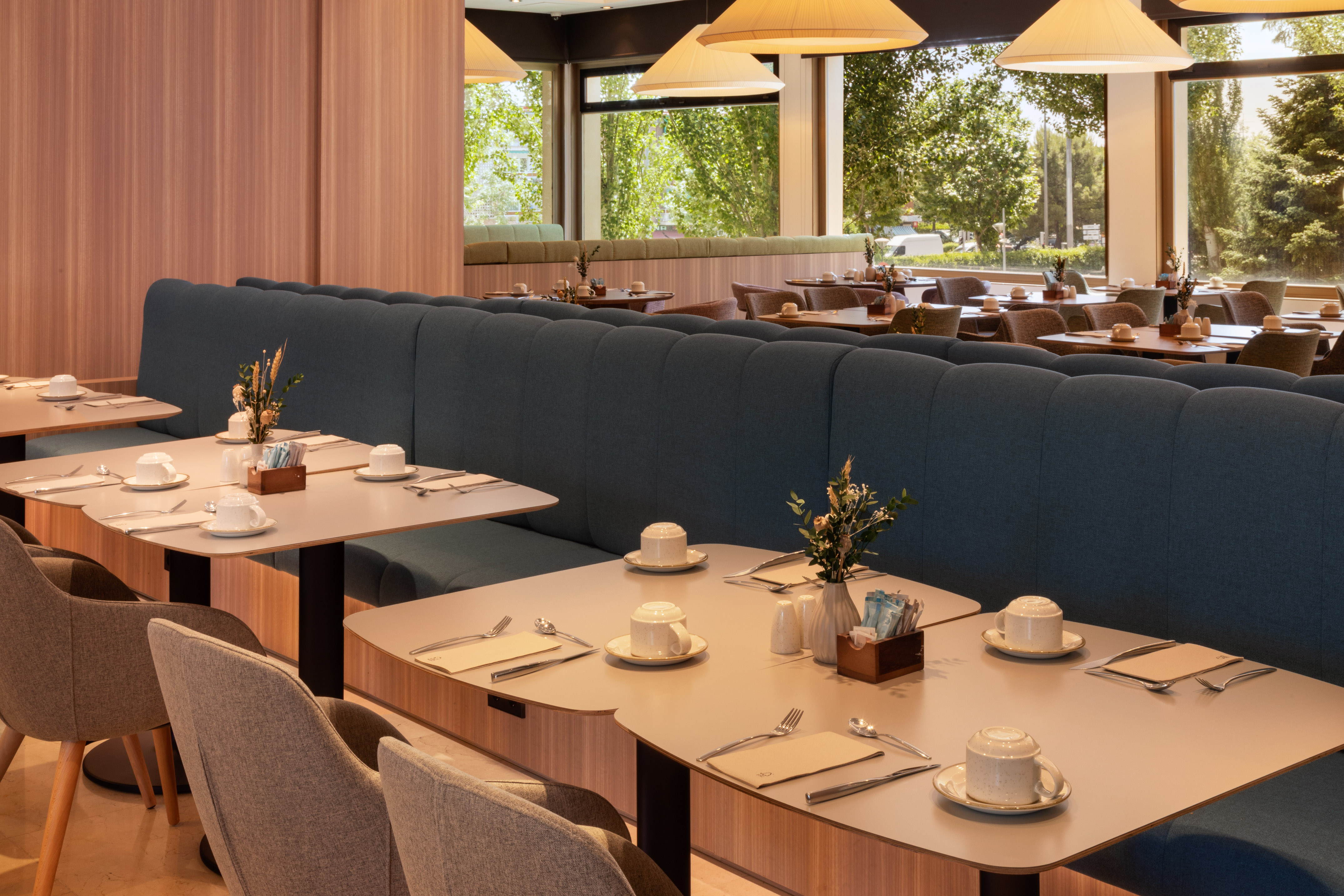 Modern restaurant dining room with blue booths, set tables, and large windows.