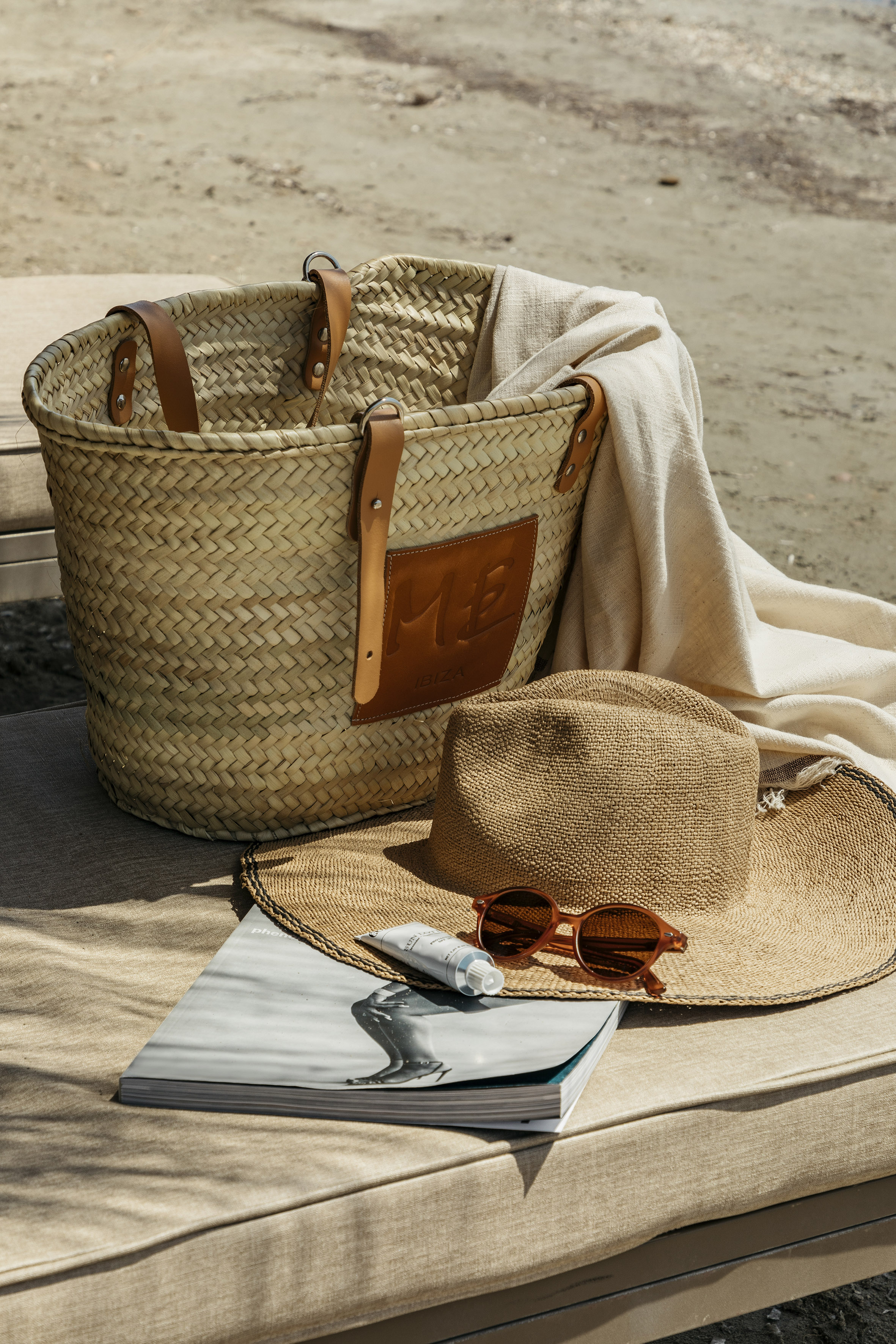 Woven beach bag, straw hat, sunglasses, sunscreen on lounger.