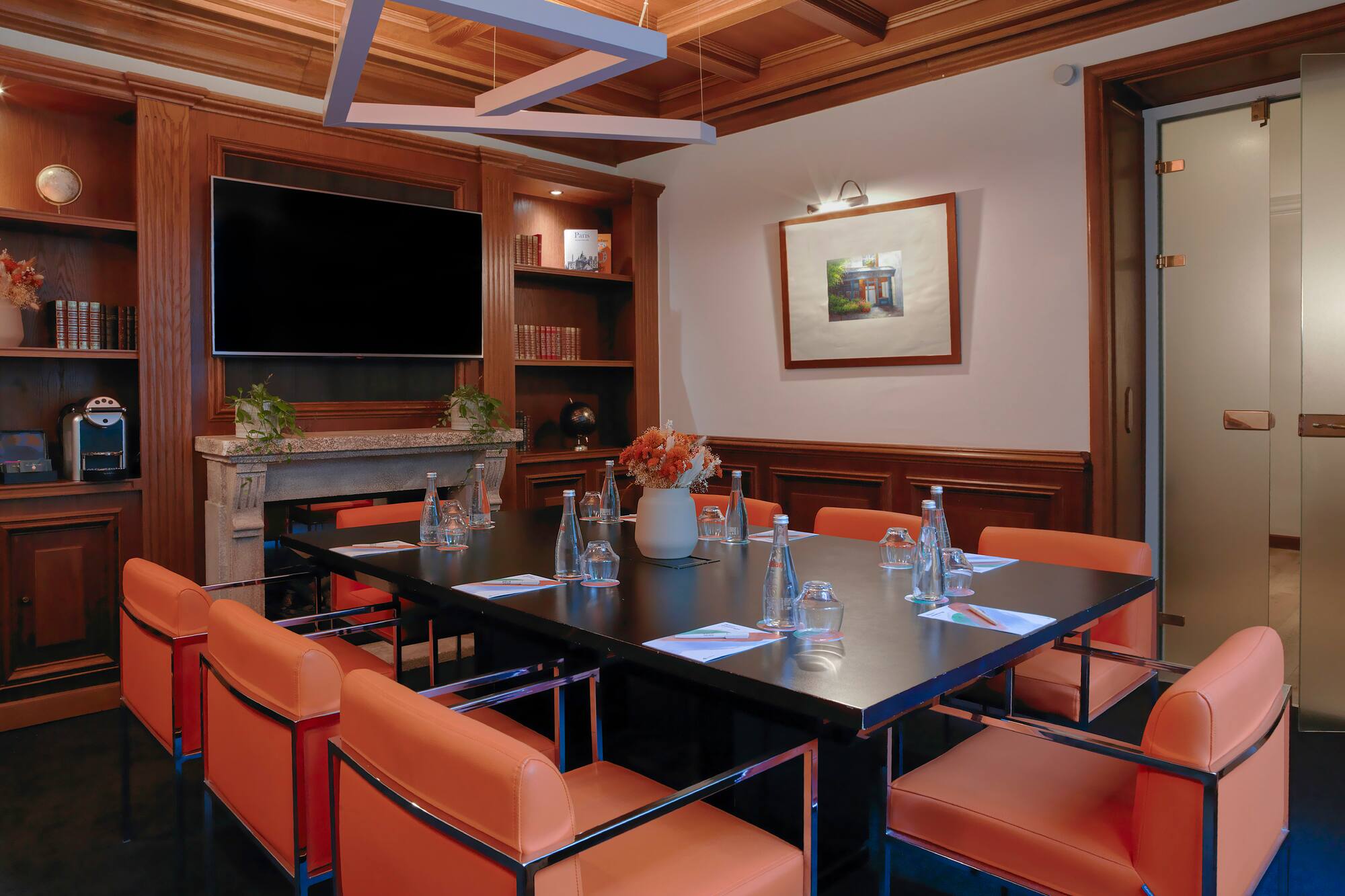 Modern meeting room with wood panels, orange chairs, TV, and conference table.
