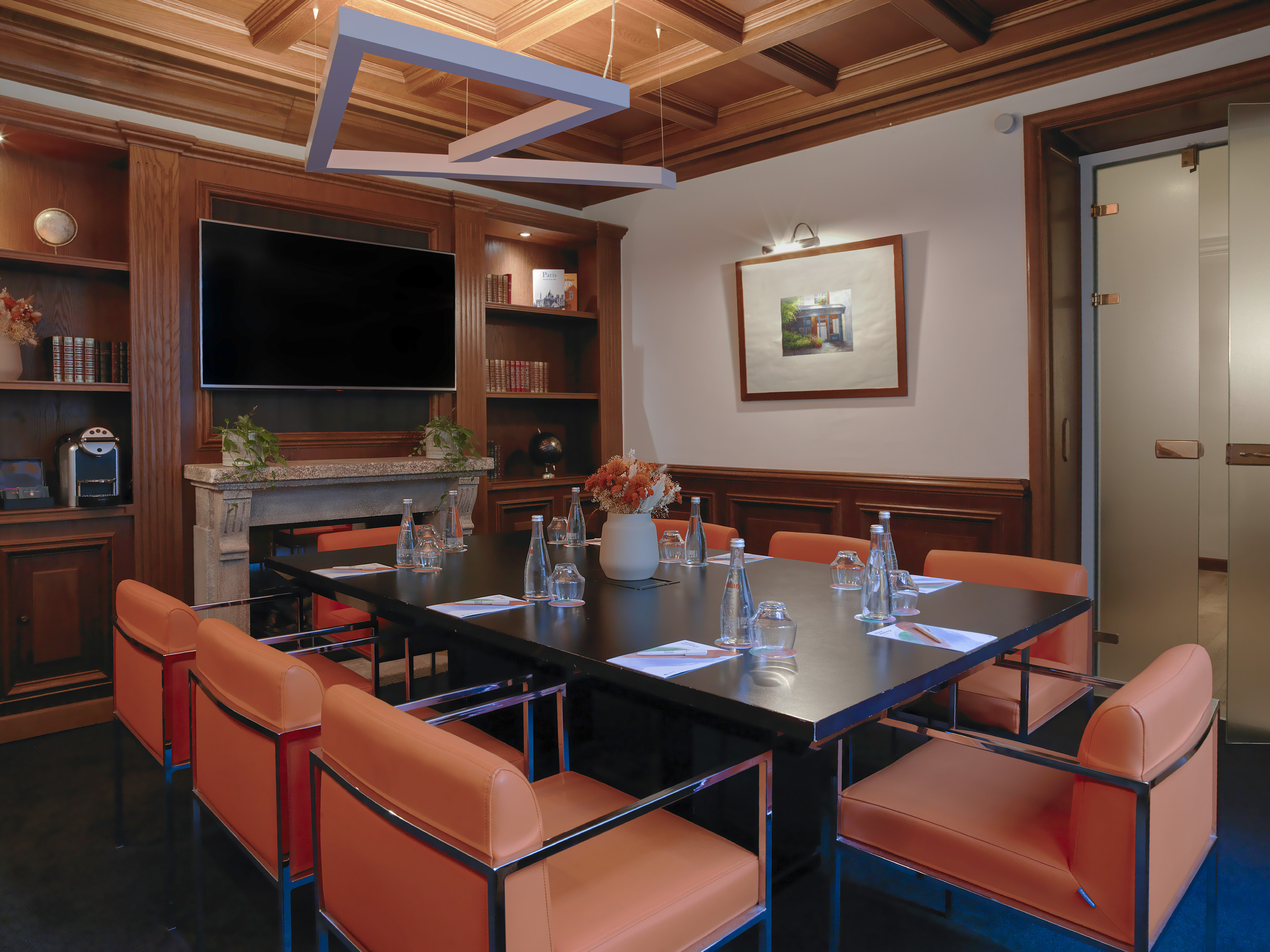 Modern meeting room with wood panels, orange chairs, TV, and conference table.