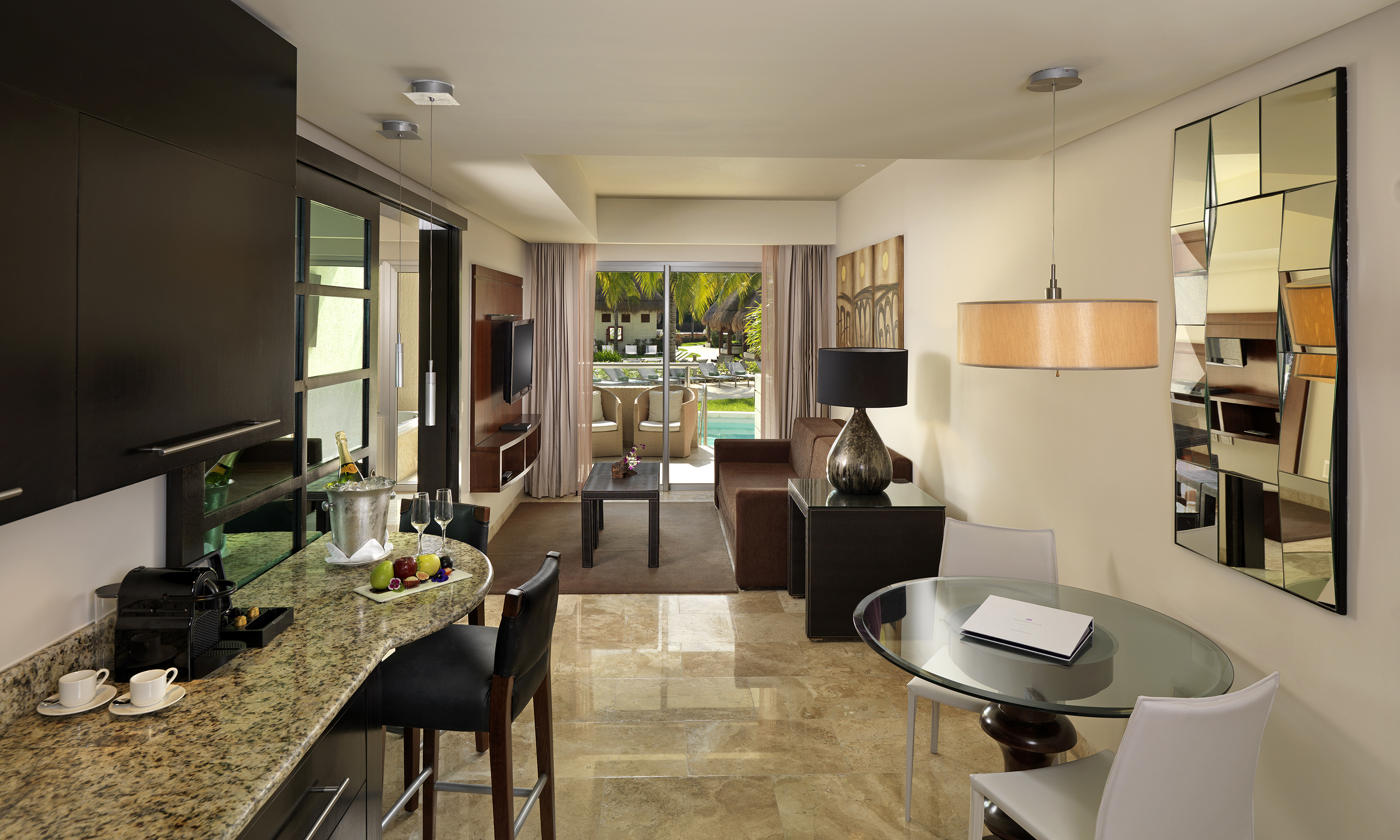 Modern luxury suite: living room, kitchen bar, tropical pool view.