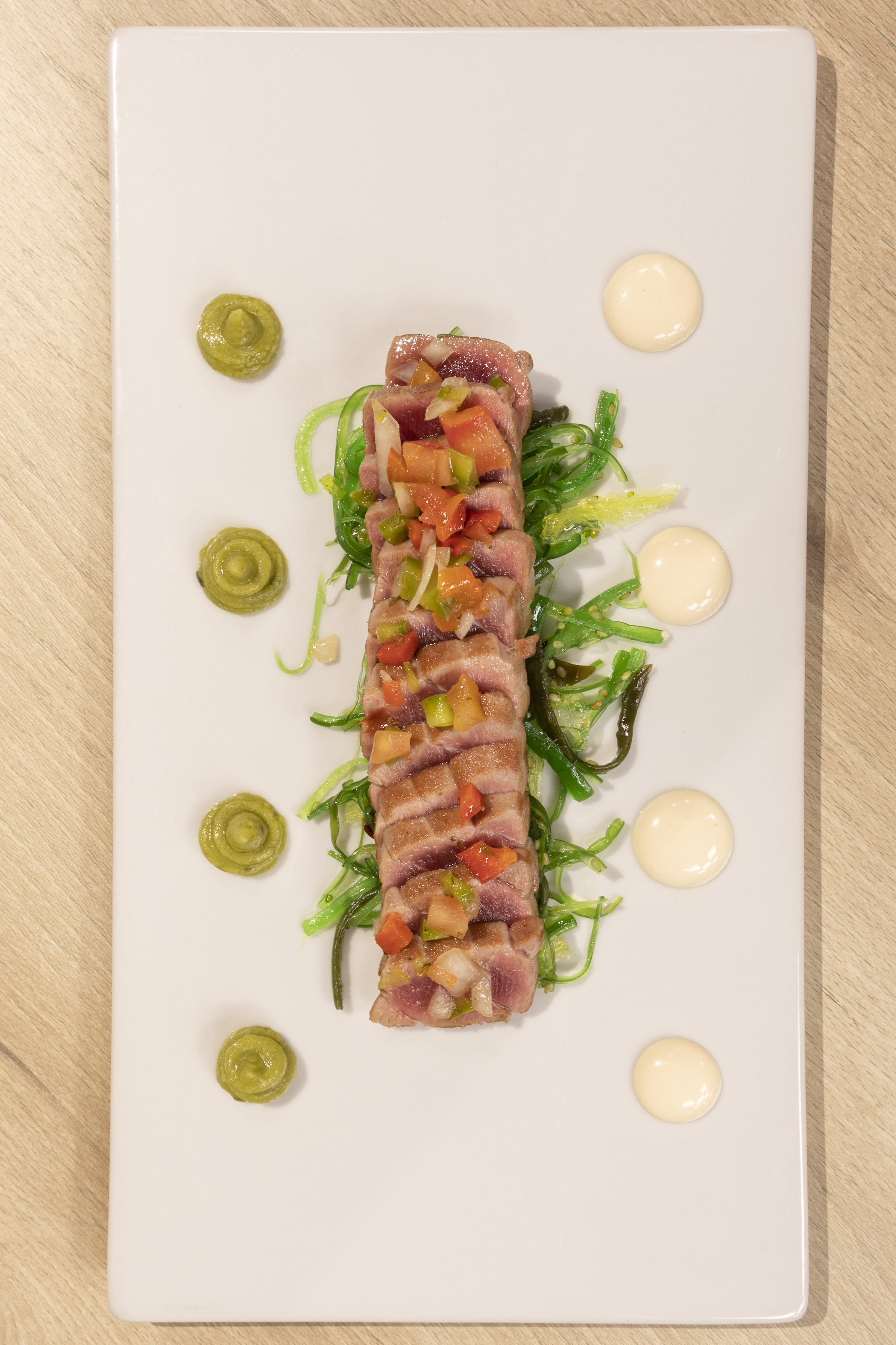 Seared tuna tataki with wakame salad, fresh salsa, and sauces on a white serving plate.