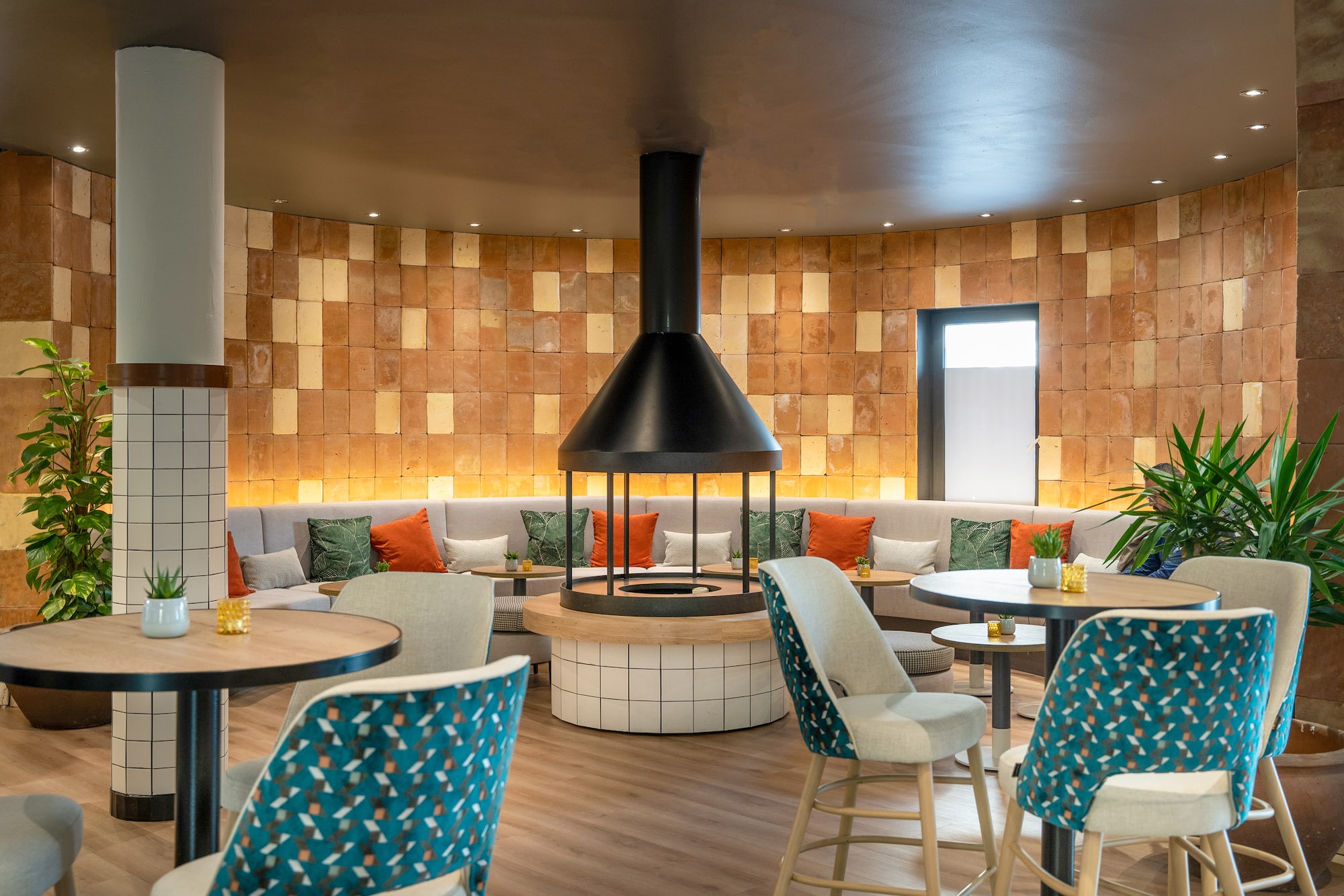 Modern hotel lounge with circular fireplace, curved brick wall, and contemporary seating.