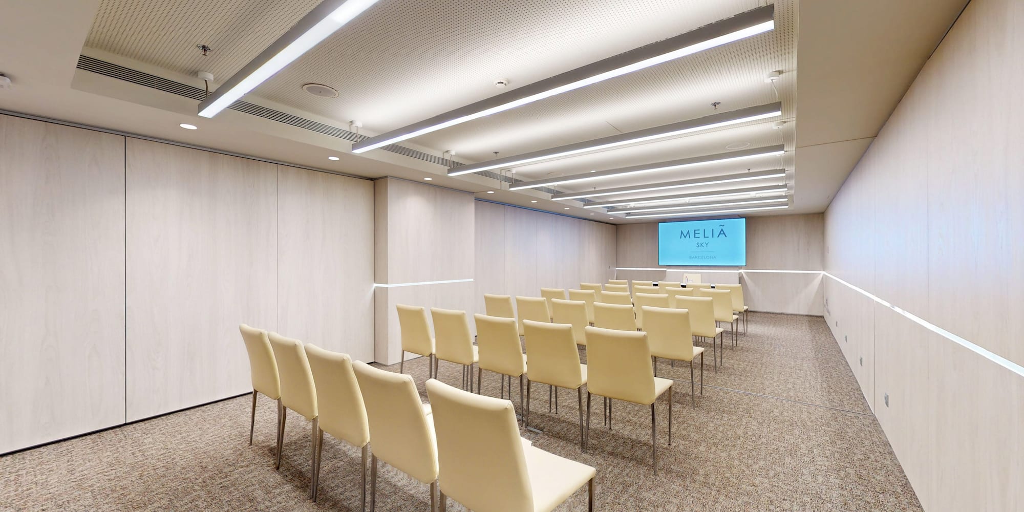 Melia Sky Barcelona meeting room with rows of chairs and screen.