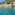 Sparkling turquoise water by a rugged rocky coast and green hillside.