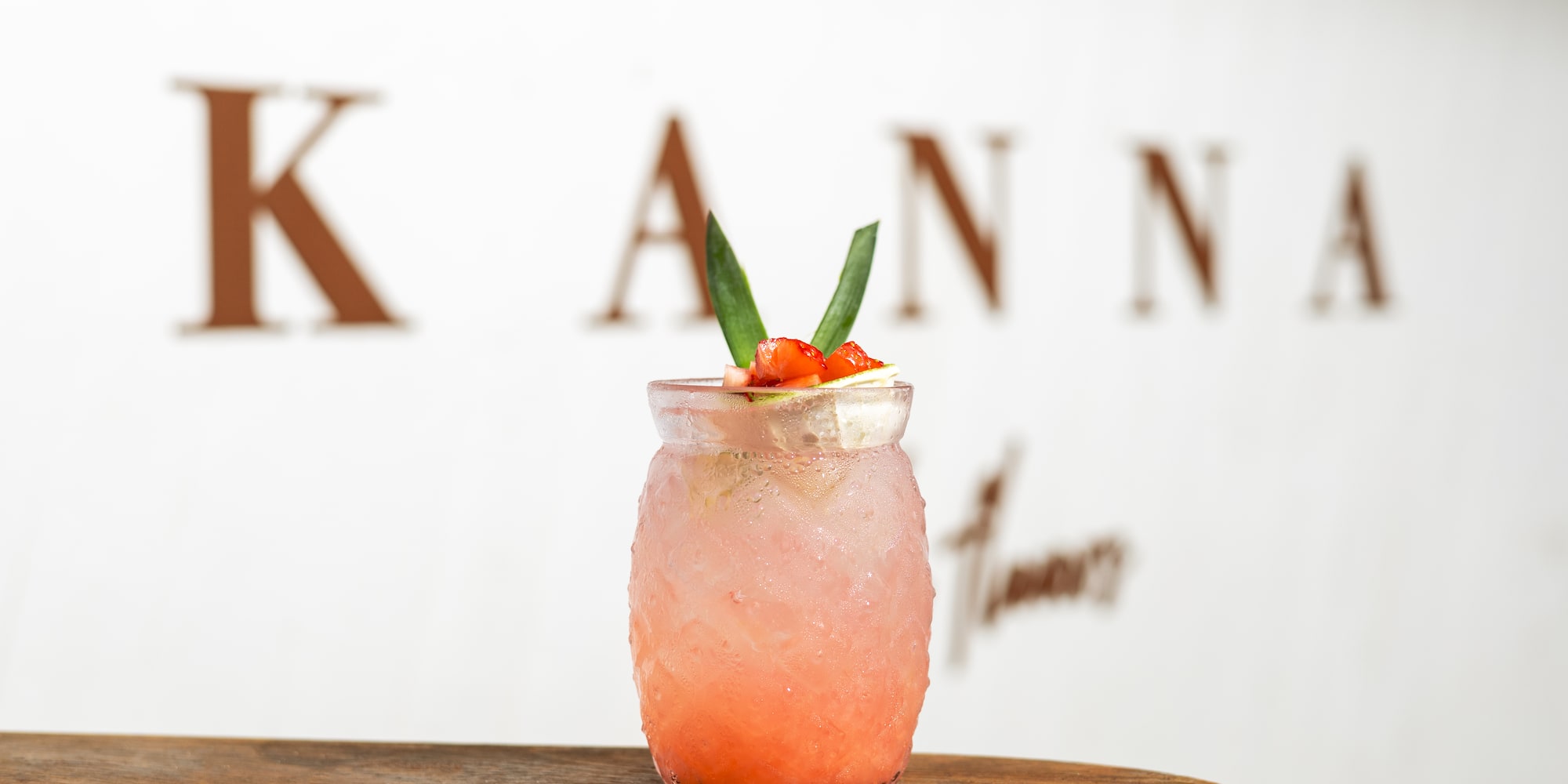 Iced strawberry Kanna drink with green garnish on wooden surface.