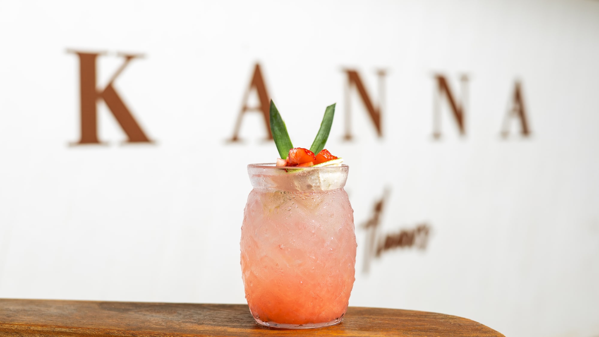 Iced strawberry Kanna drink with green garnish on wooden surface.