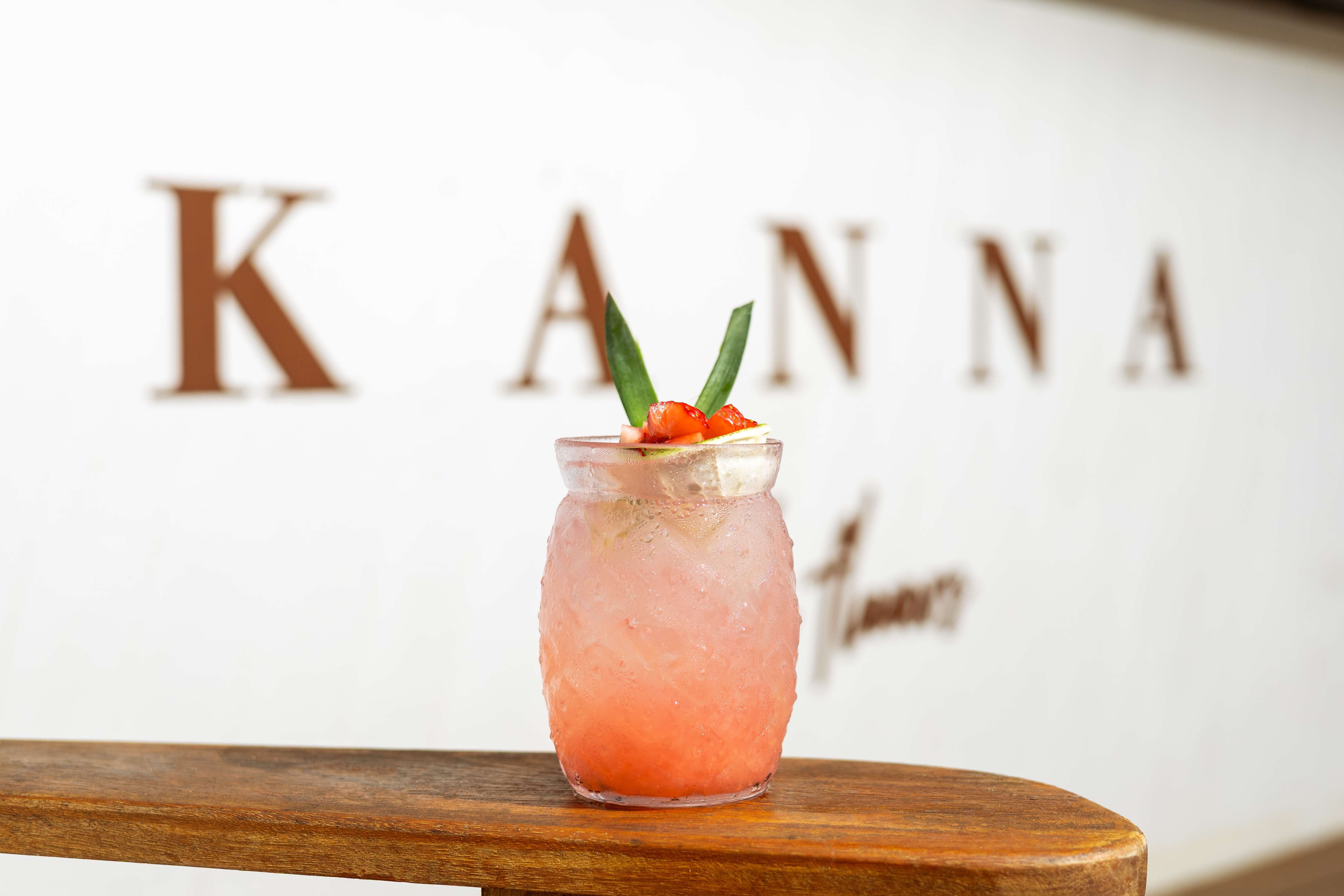 Iced strawberry Kanna drink with green garnish on wooden surface.
