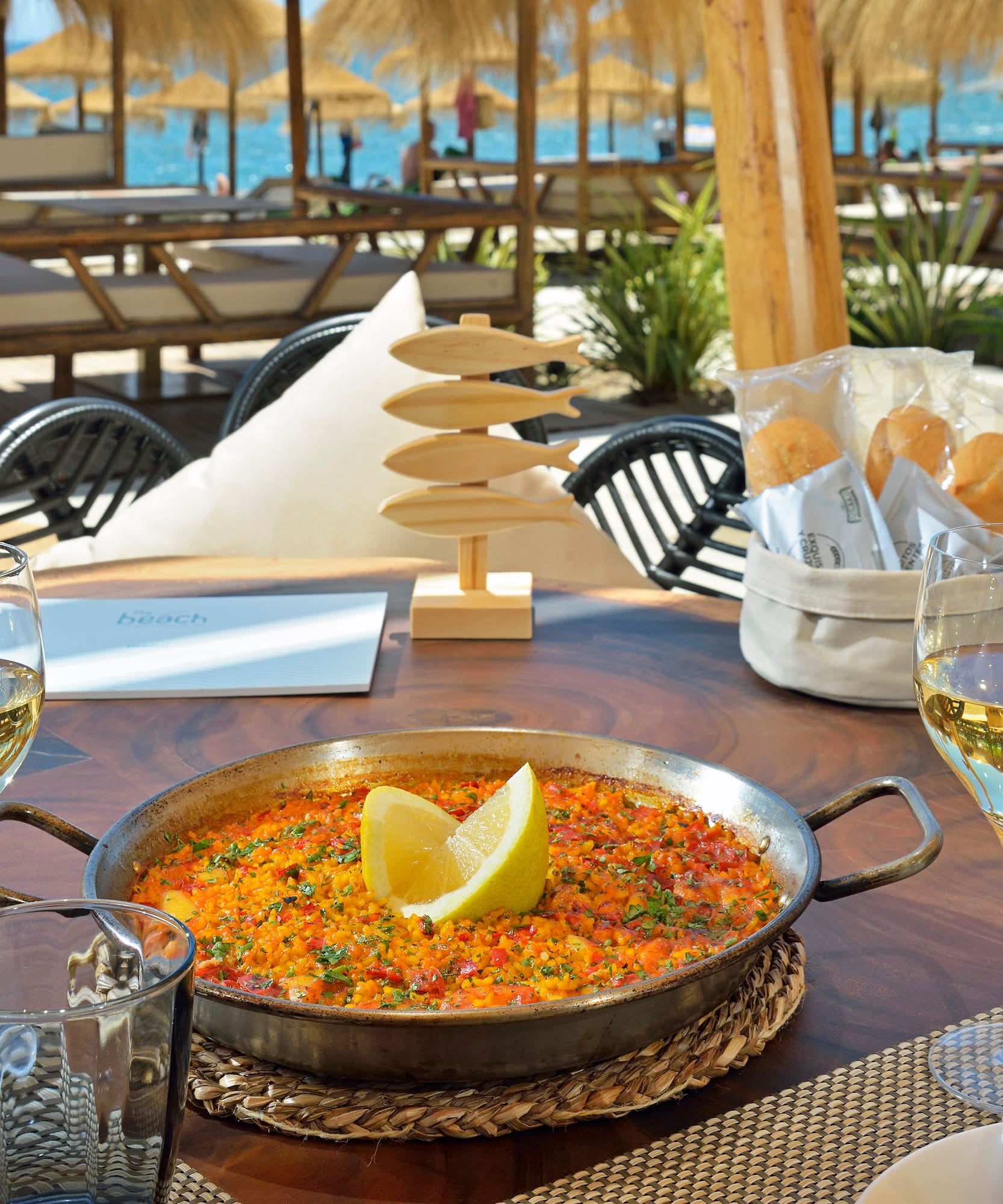 a pan of food on a table with wine glasses and a beach