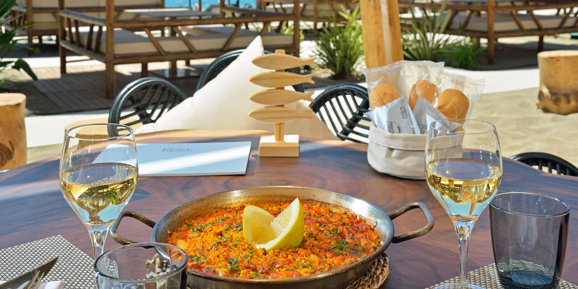 Paella, white wine at beach restaurant table; outdoor Mediterranean dining.