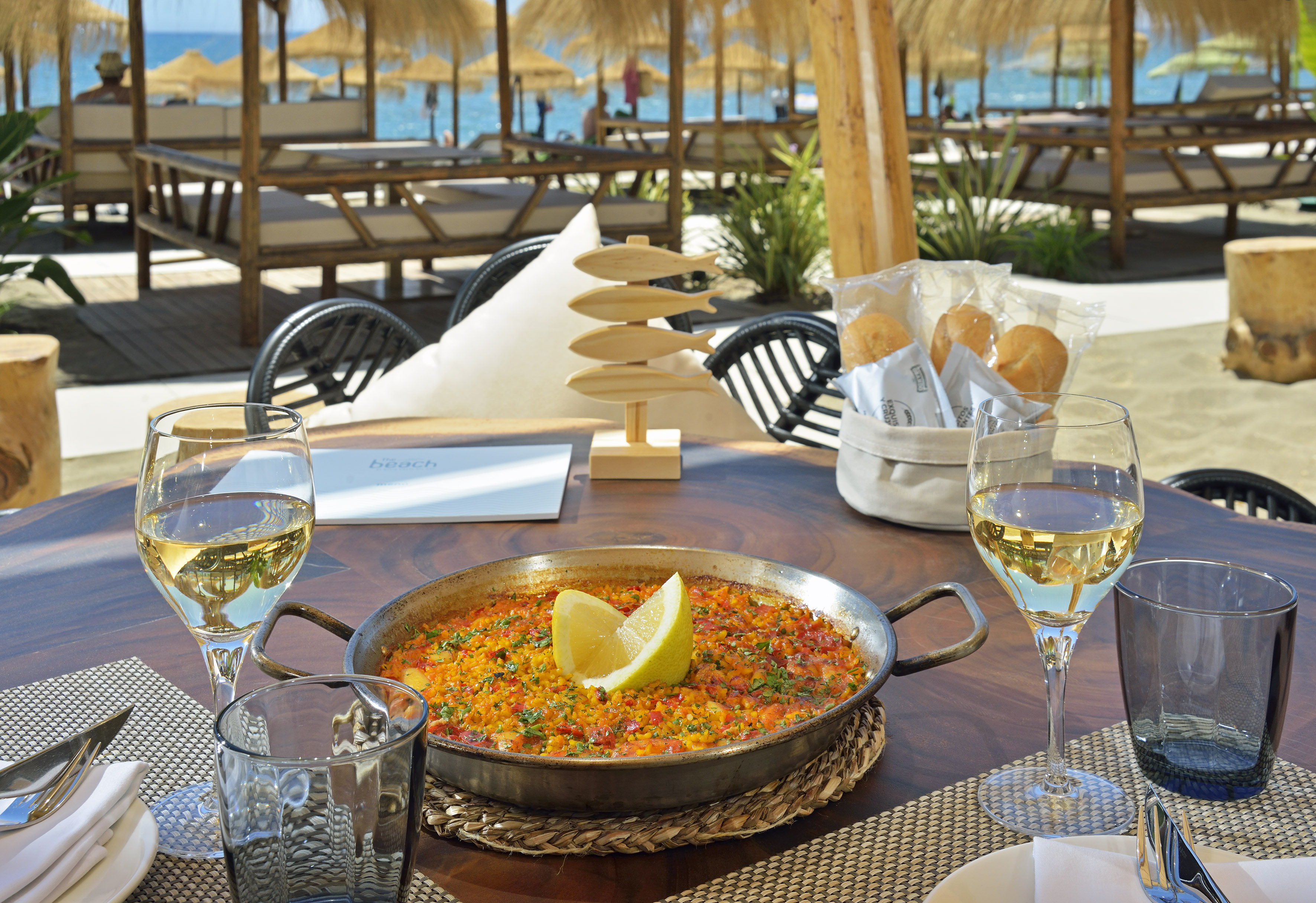 Paella, white wine at beach restaurant table; outdoor Mediterranean dining.