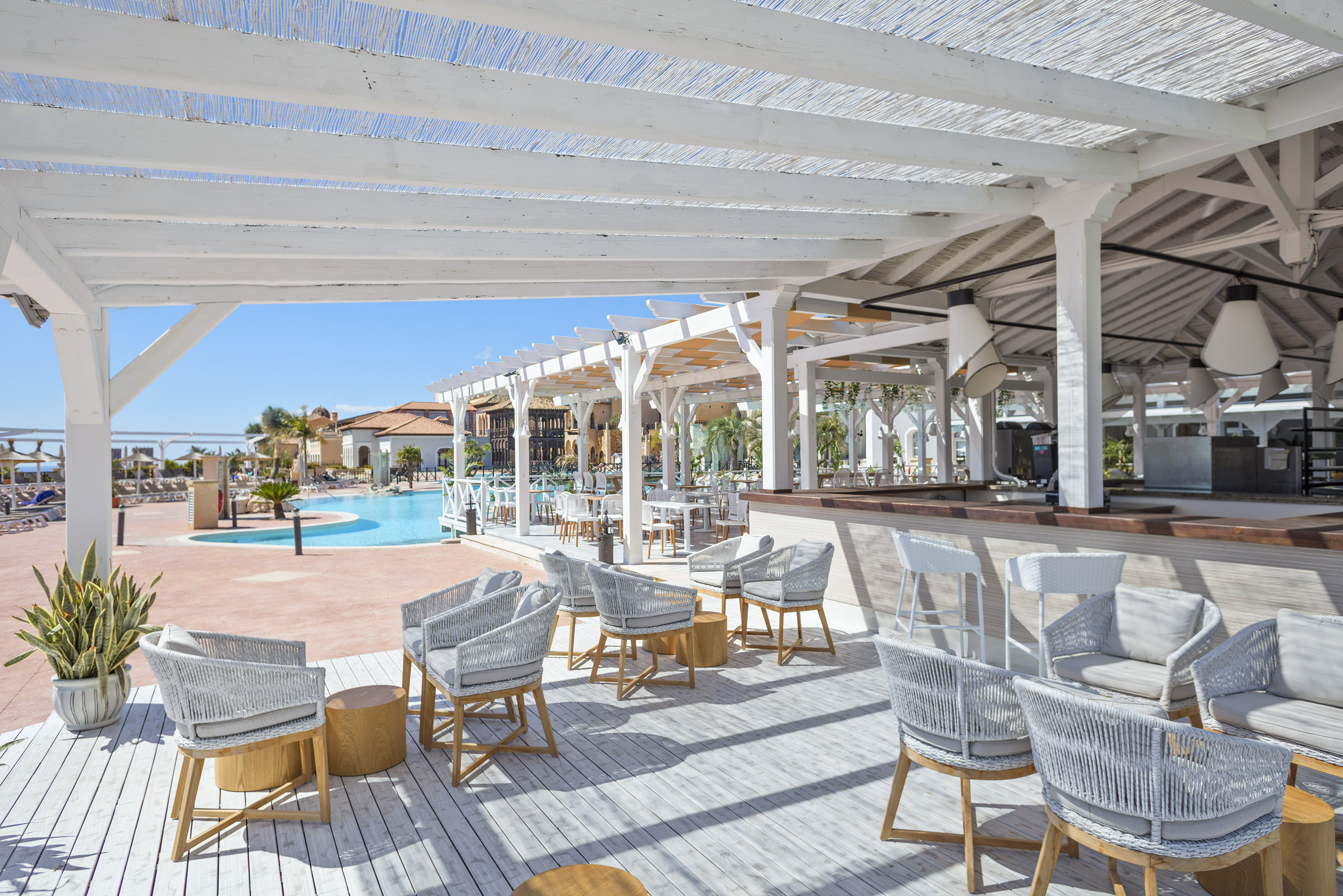 Resort poolside bar lounge under a white pergola with modern grey seating.