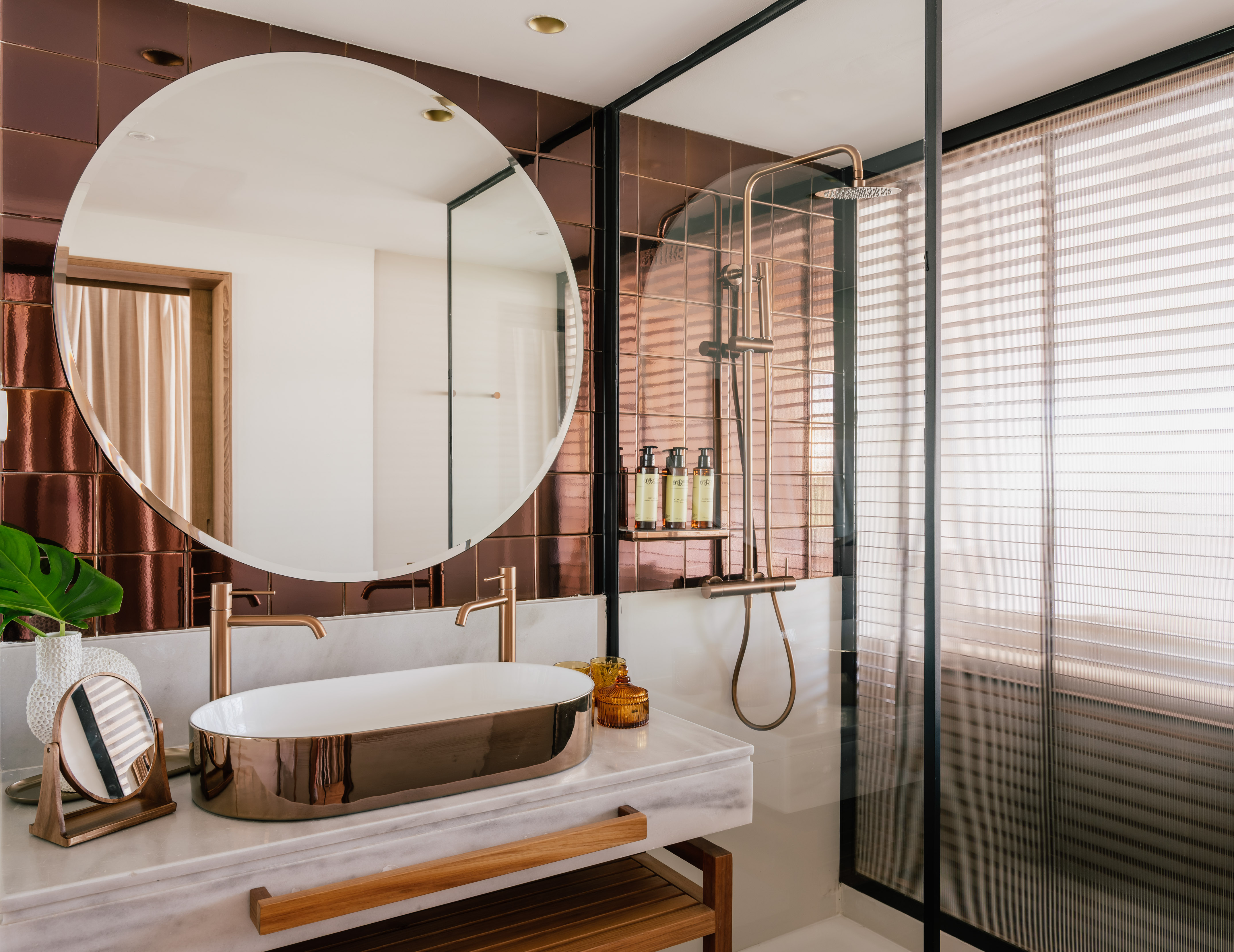 Modern bathroom with rose gold fixtures, marble vanity, and copper tiles.