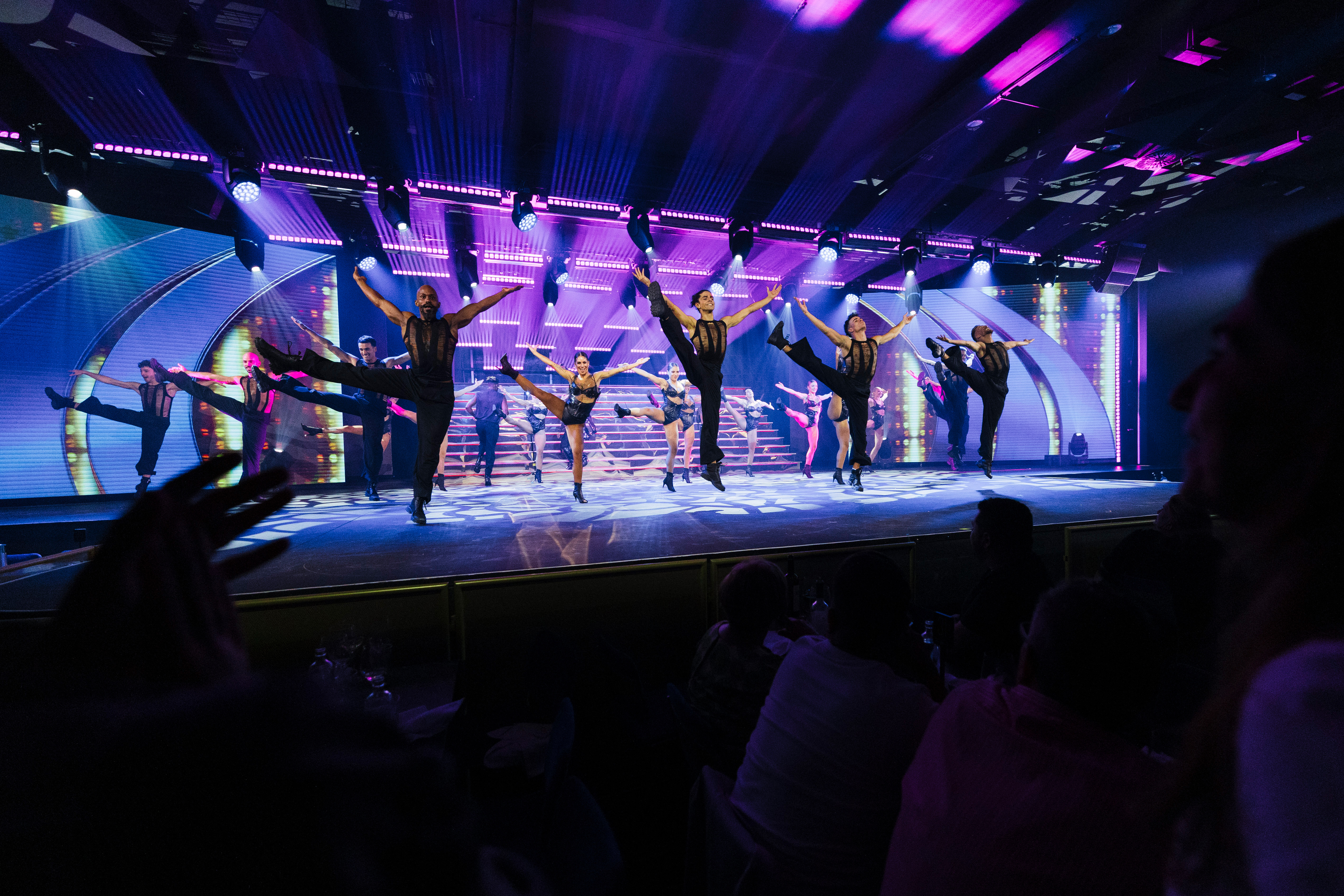 Live show: energetic dancers perform on stage with purple lights and audience.