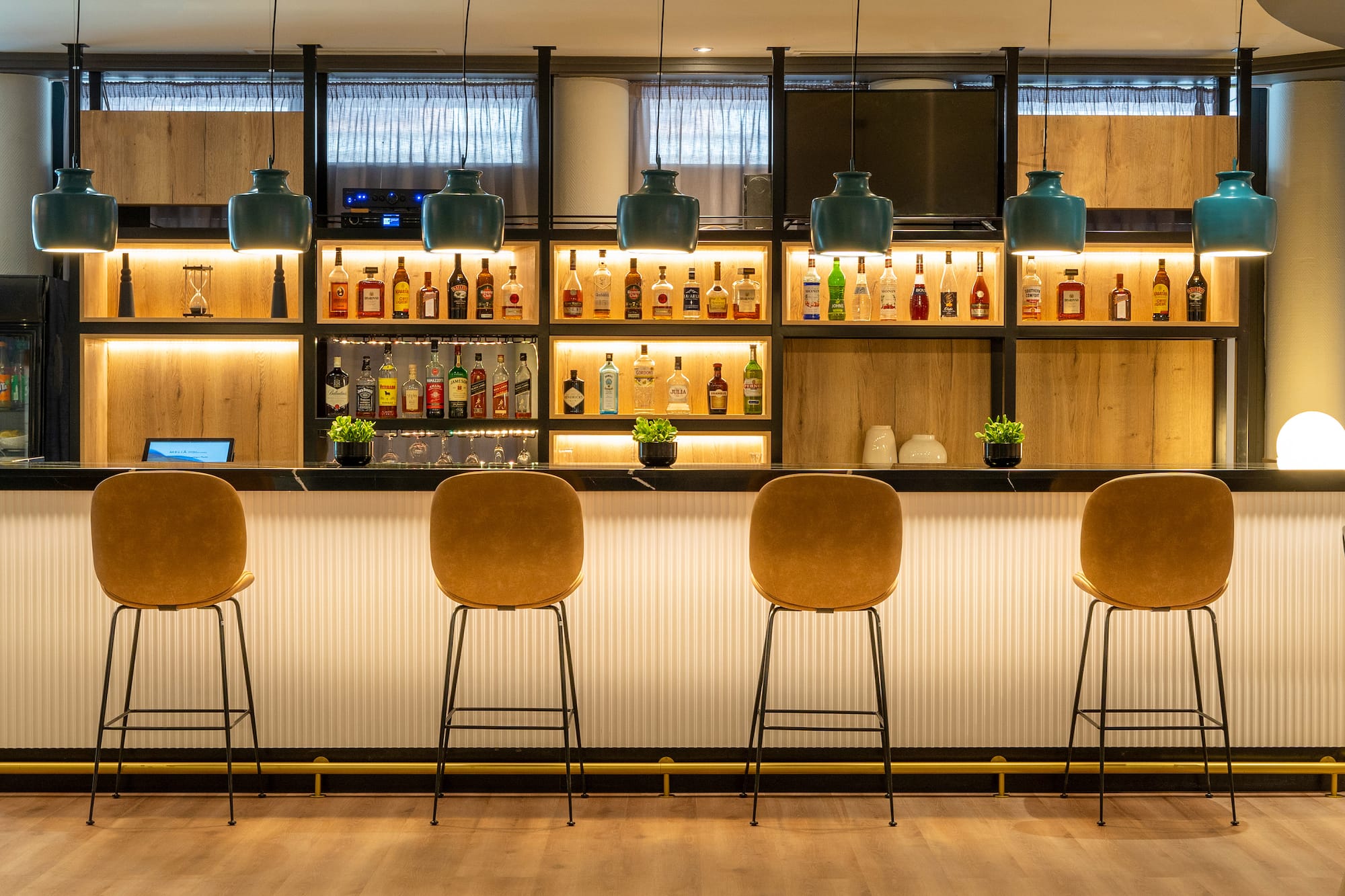 Contemporary bar with backlit liquor shelves, teal pendant lights, and brown stools.
