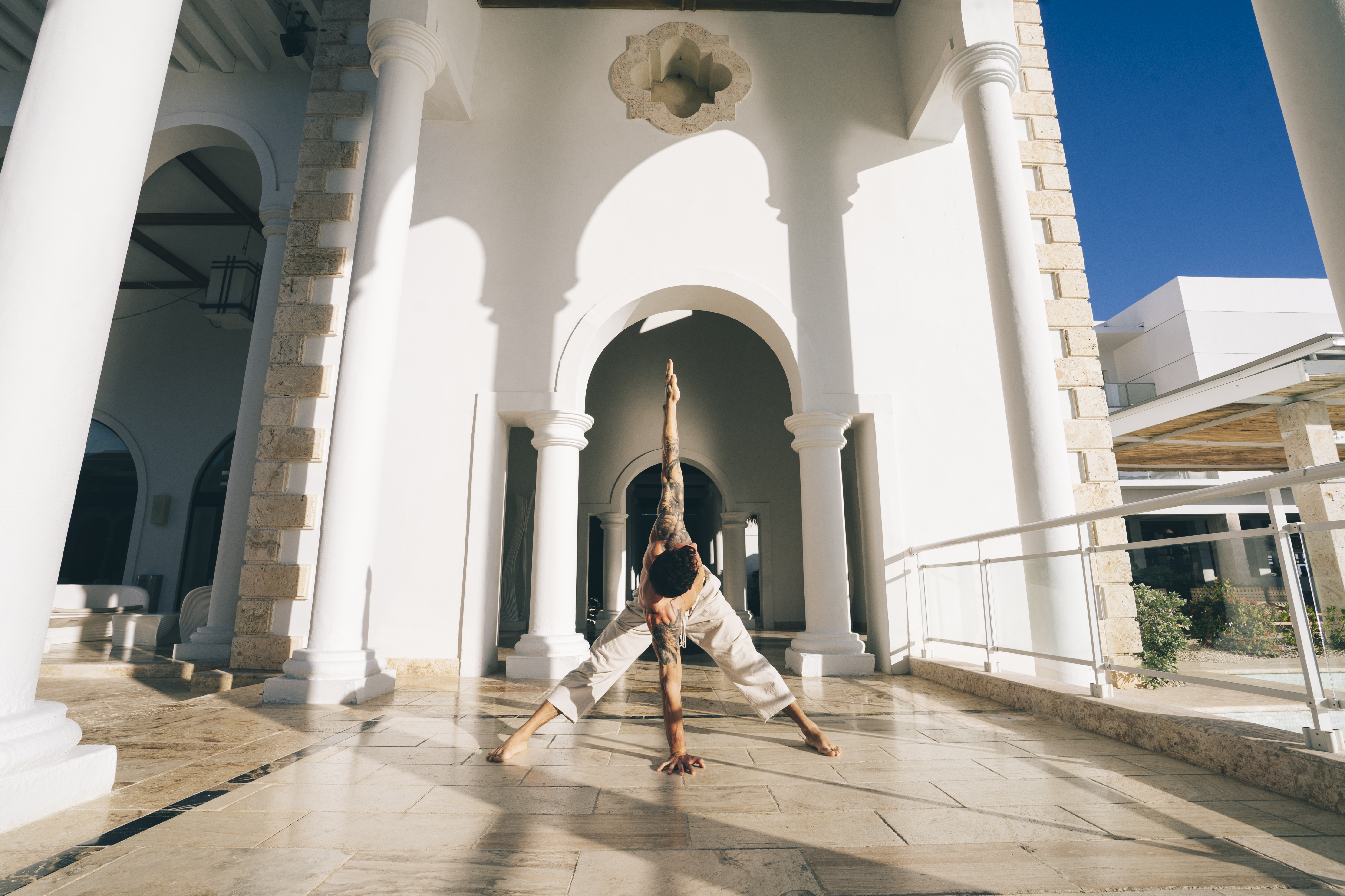 Man performing yoga pose on outdoor tiled patio with white columns and arches.