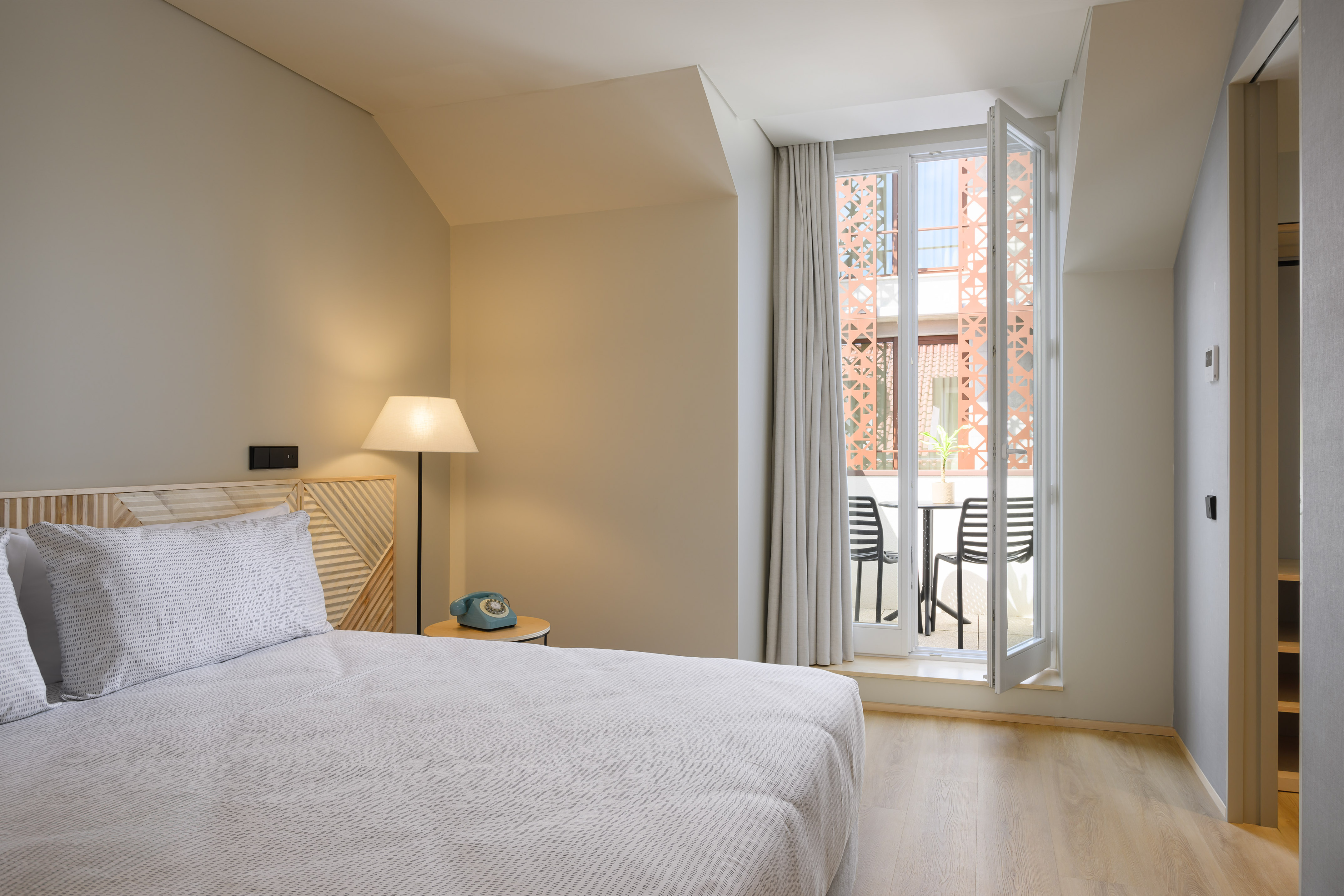 Bright modern bedroom with bed, wooden headboard, and balcony with chairs.