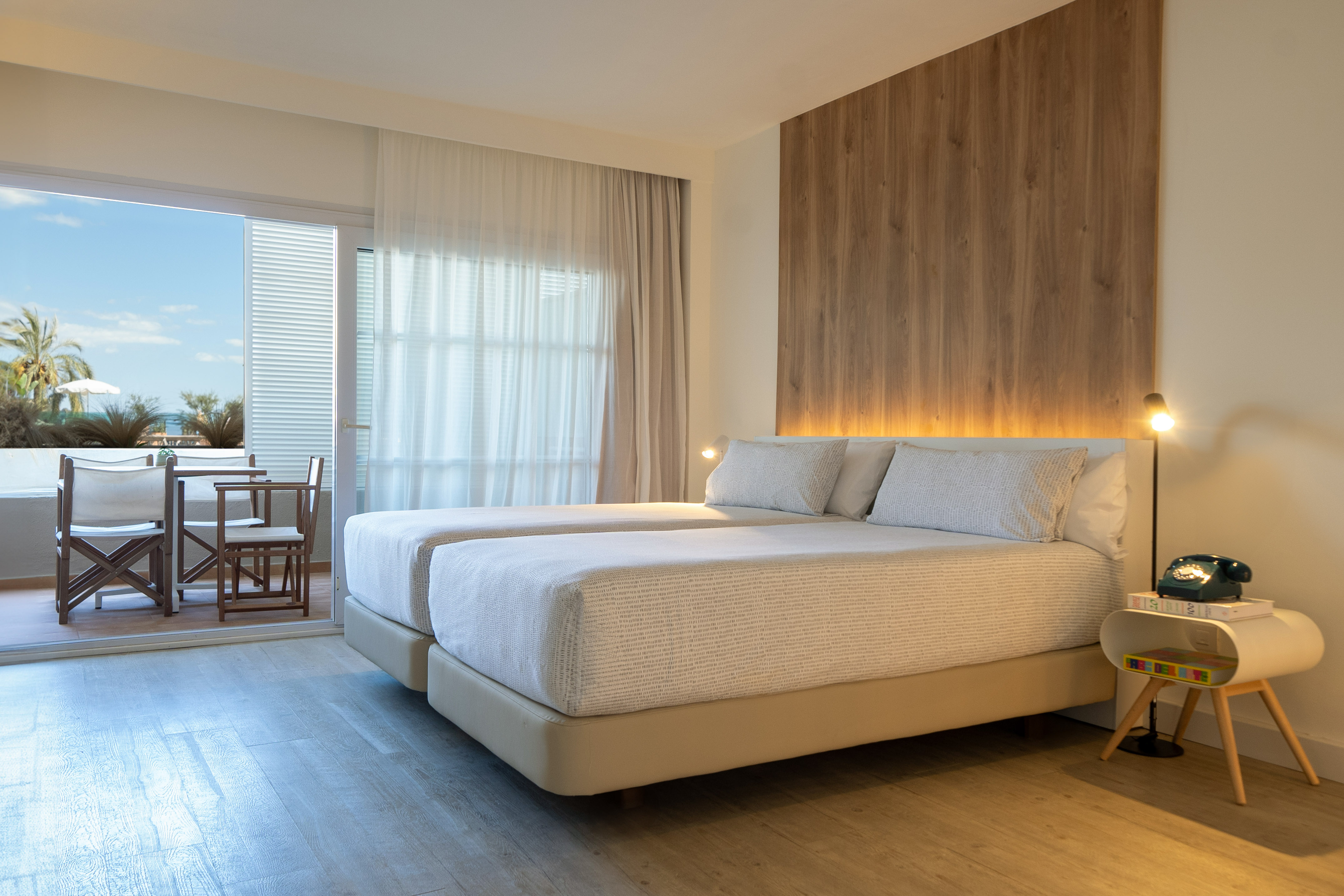 Bright hotel bedroom with twin beds, balcony overlooking the ocean and palm trees.