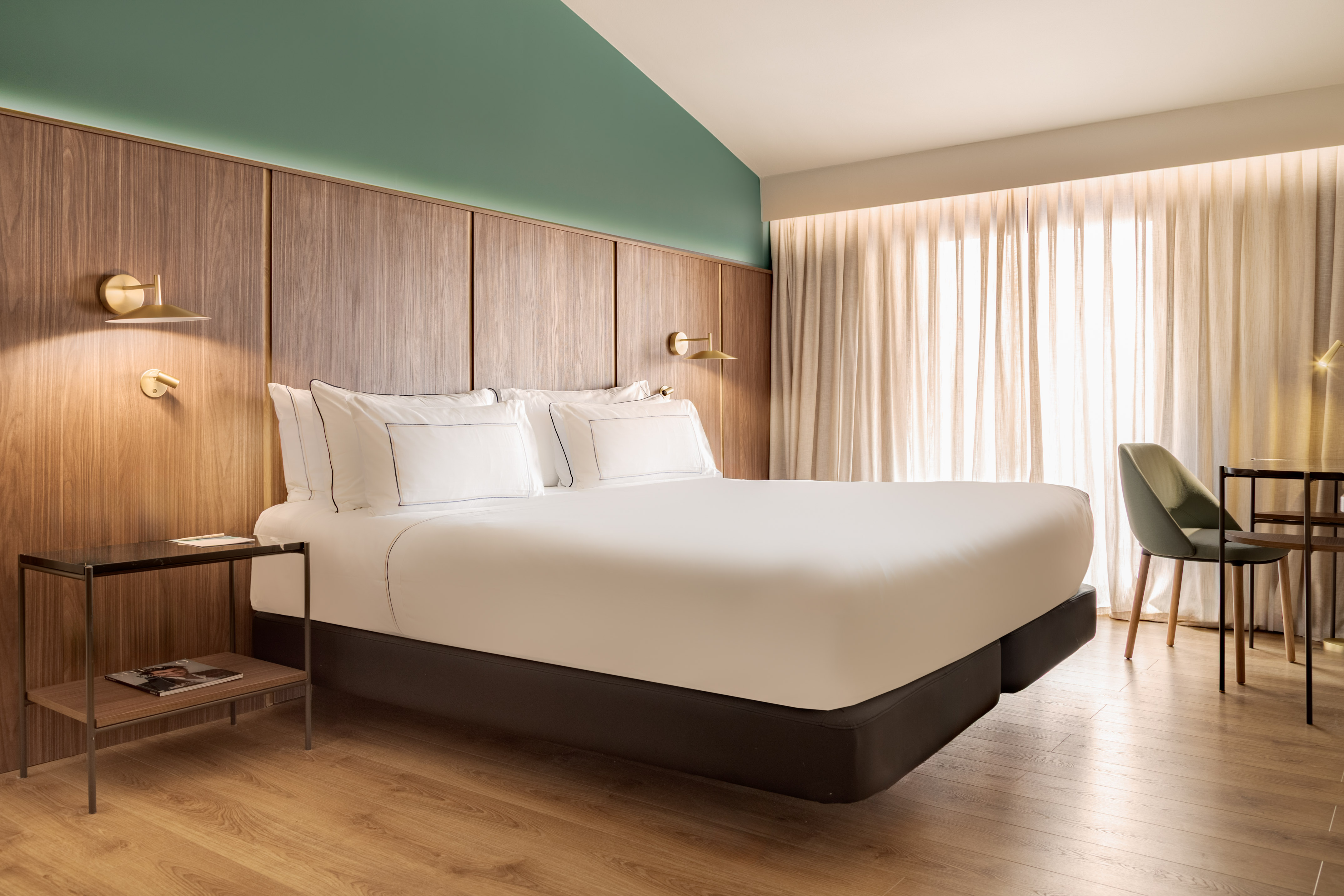 Modern hotel bedroom with wood panel headboard, green accent wall, and desk.
