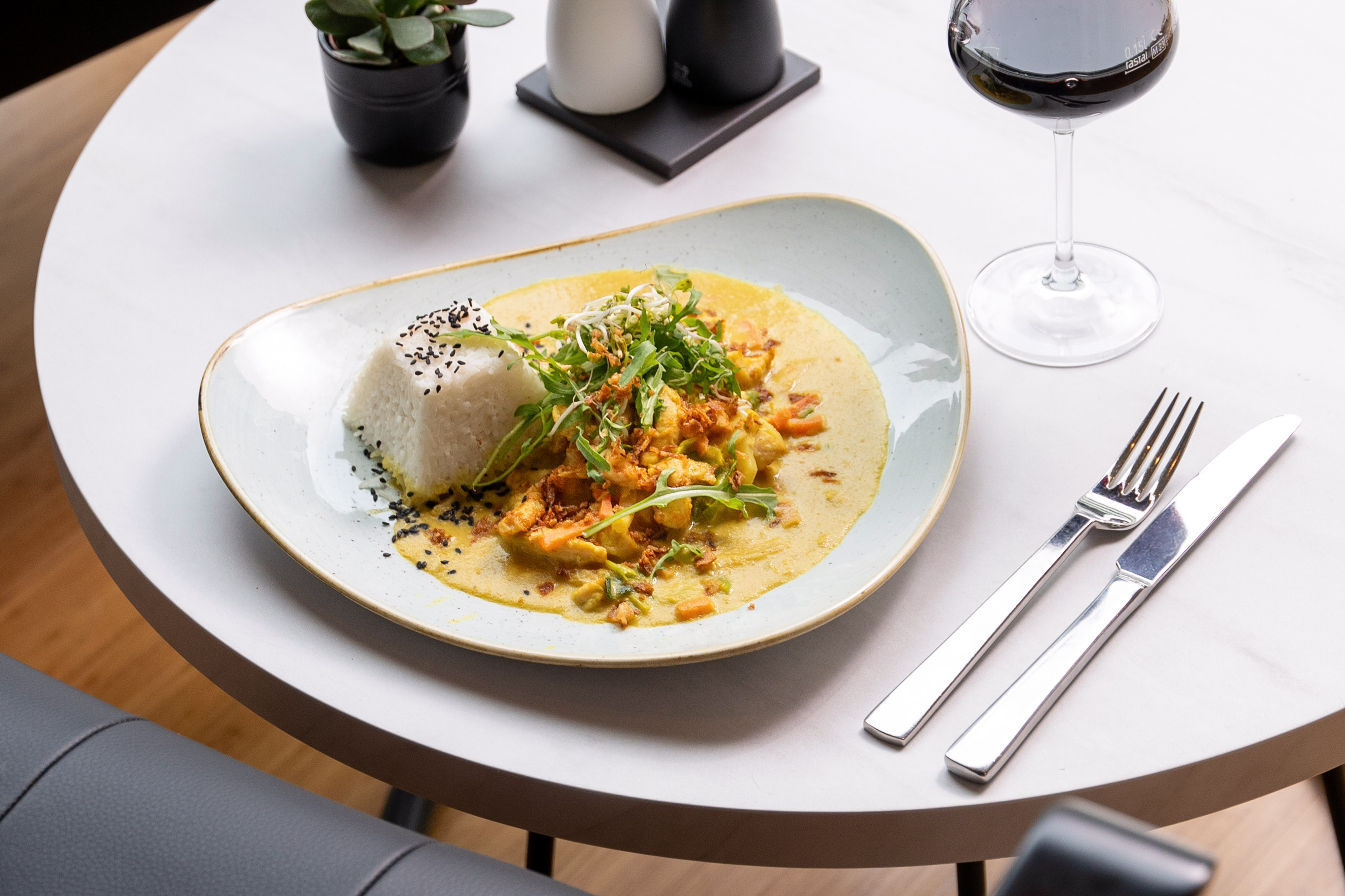 Creamy yellow curry with rice, sesame, fresh greens, and red wine on table.