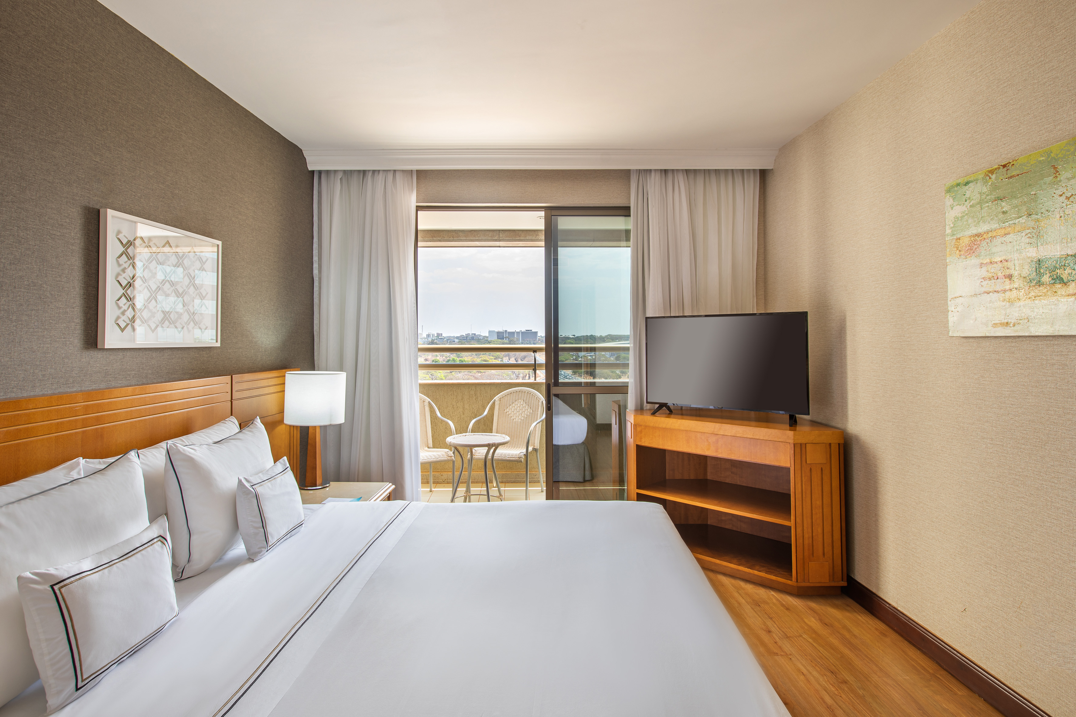Modern hotel bedroom with king bed, flat-screen TV, and balcony city view.