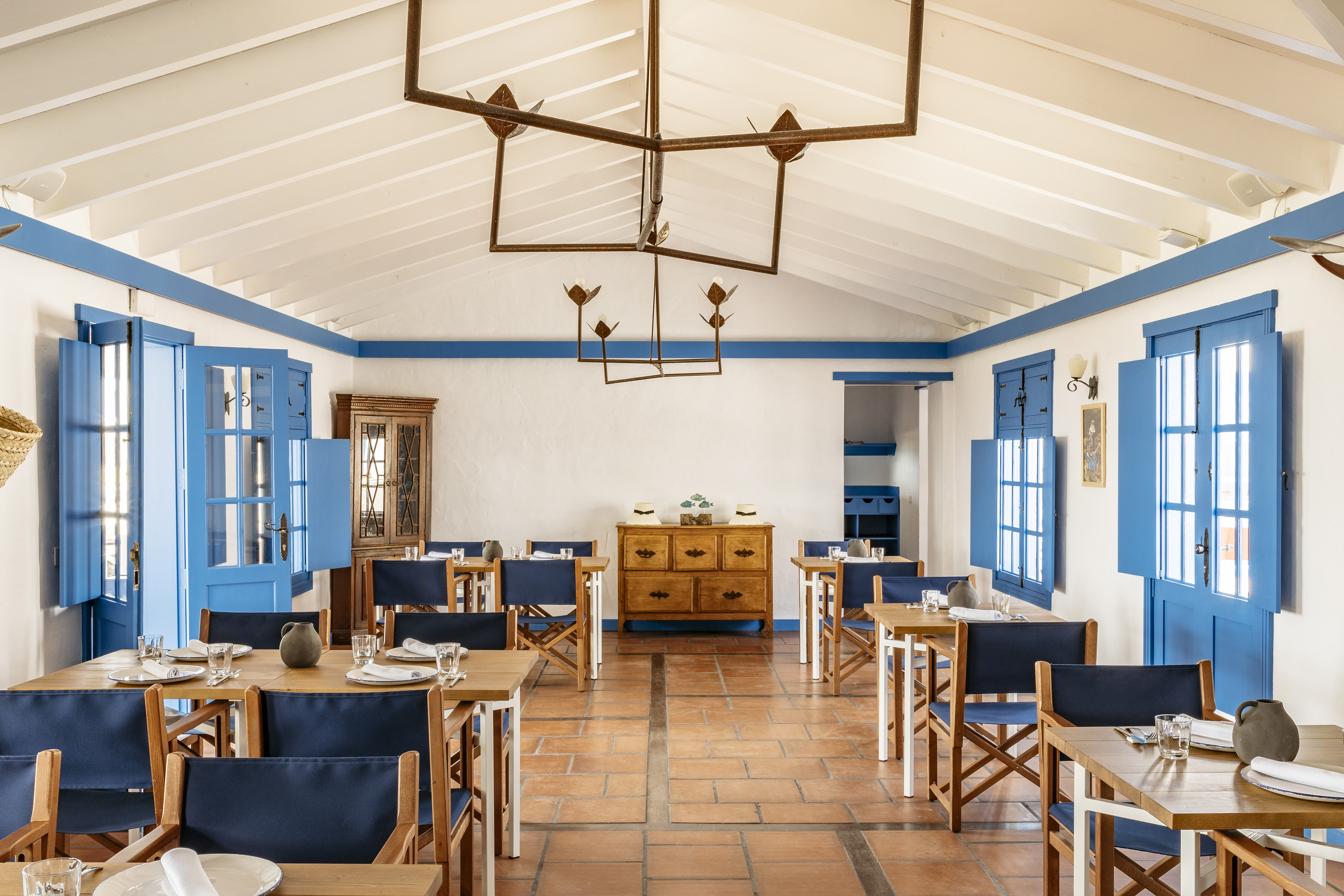 Mediterranean dining room with blue shutters, white walls, terracotta floor.