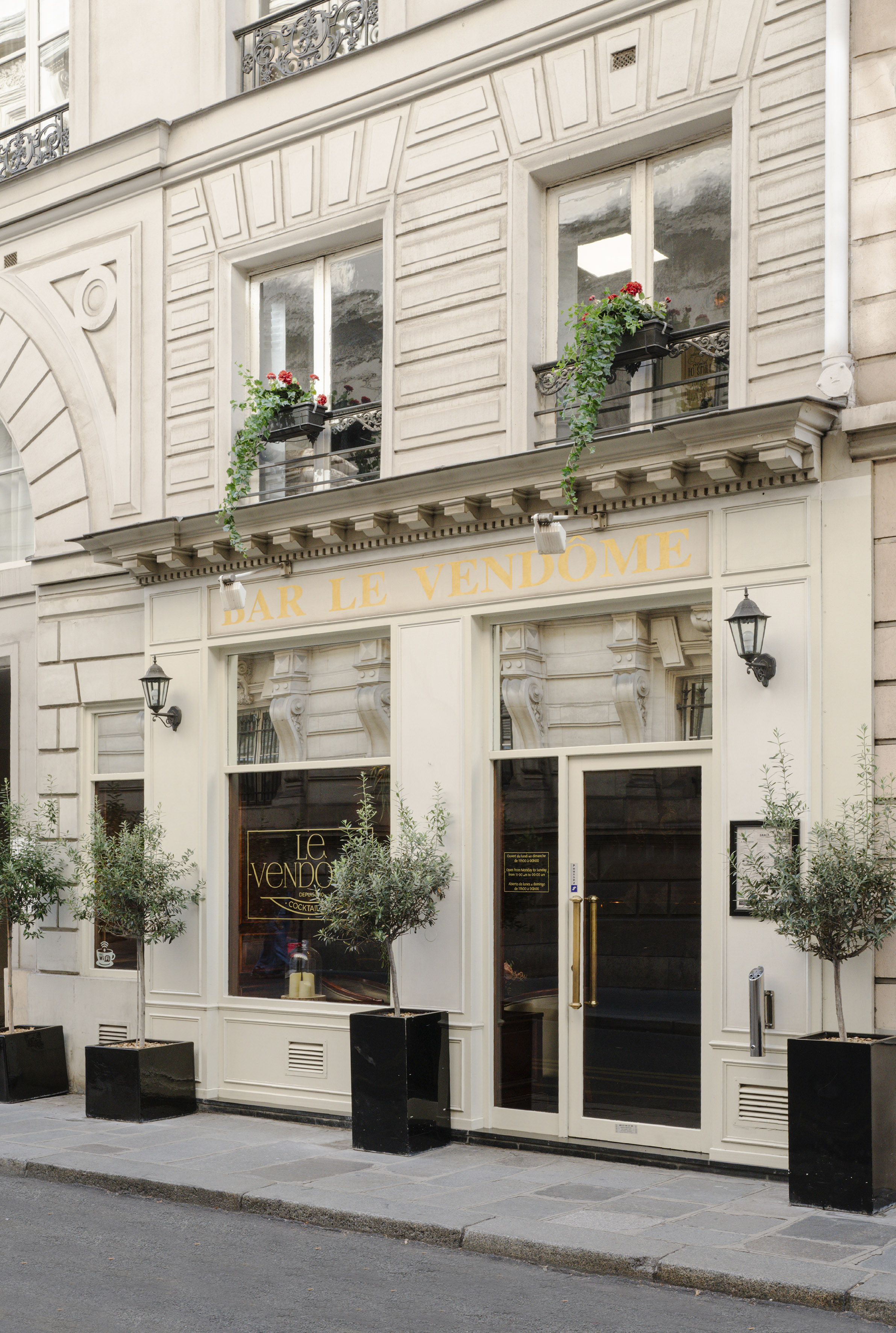 Bar Le Vendome facade in Paris with gold sign, planters, and red flowers.