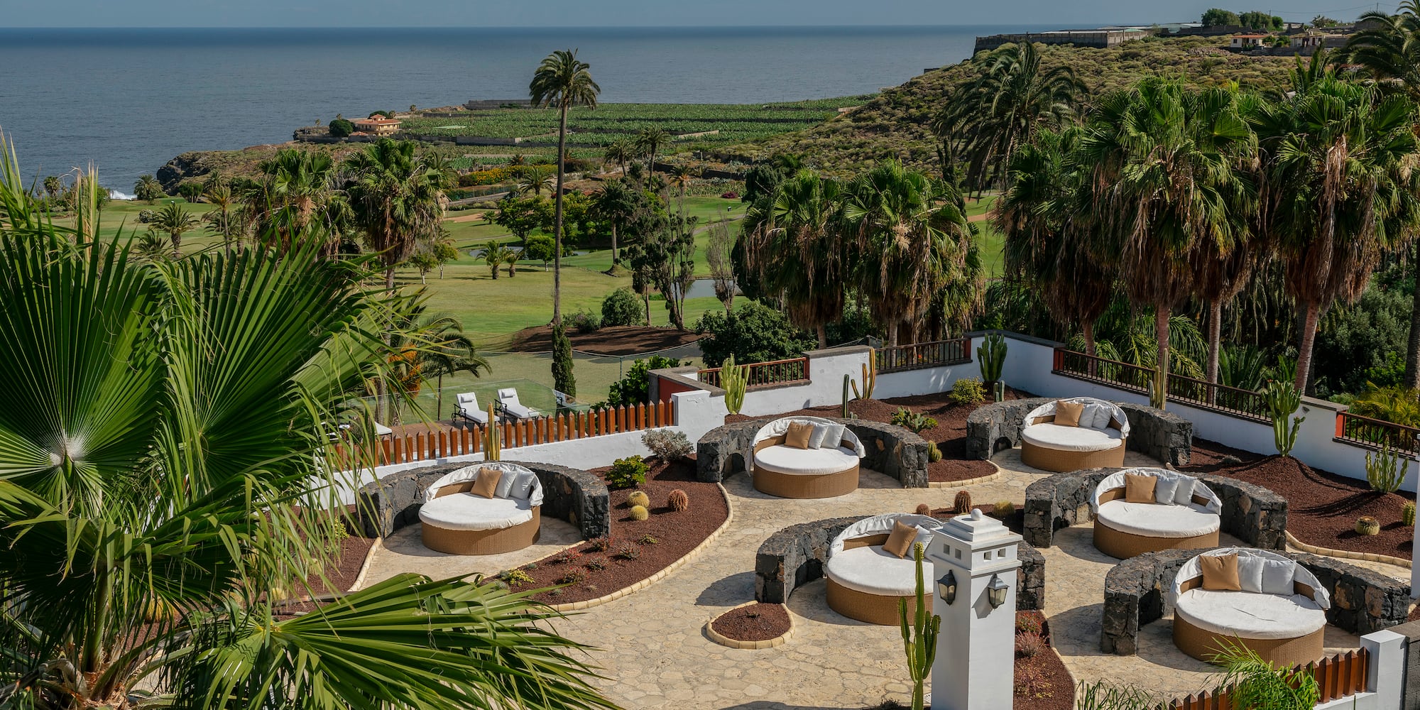 Luxury resort patio with round daybeds overlooking golf course and ocean.