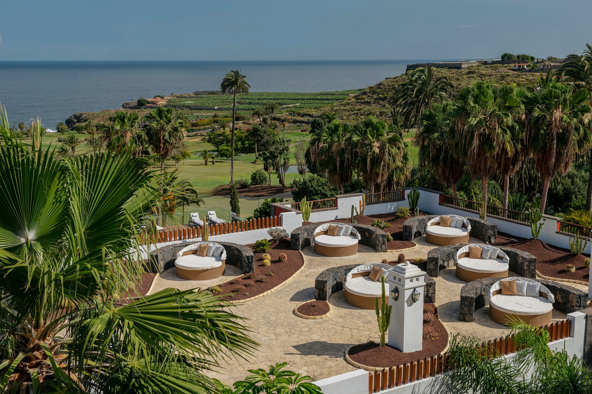 Luxury resort patio with round daybeds overlooking golf course and ocean.