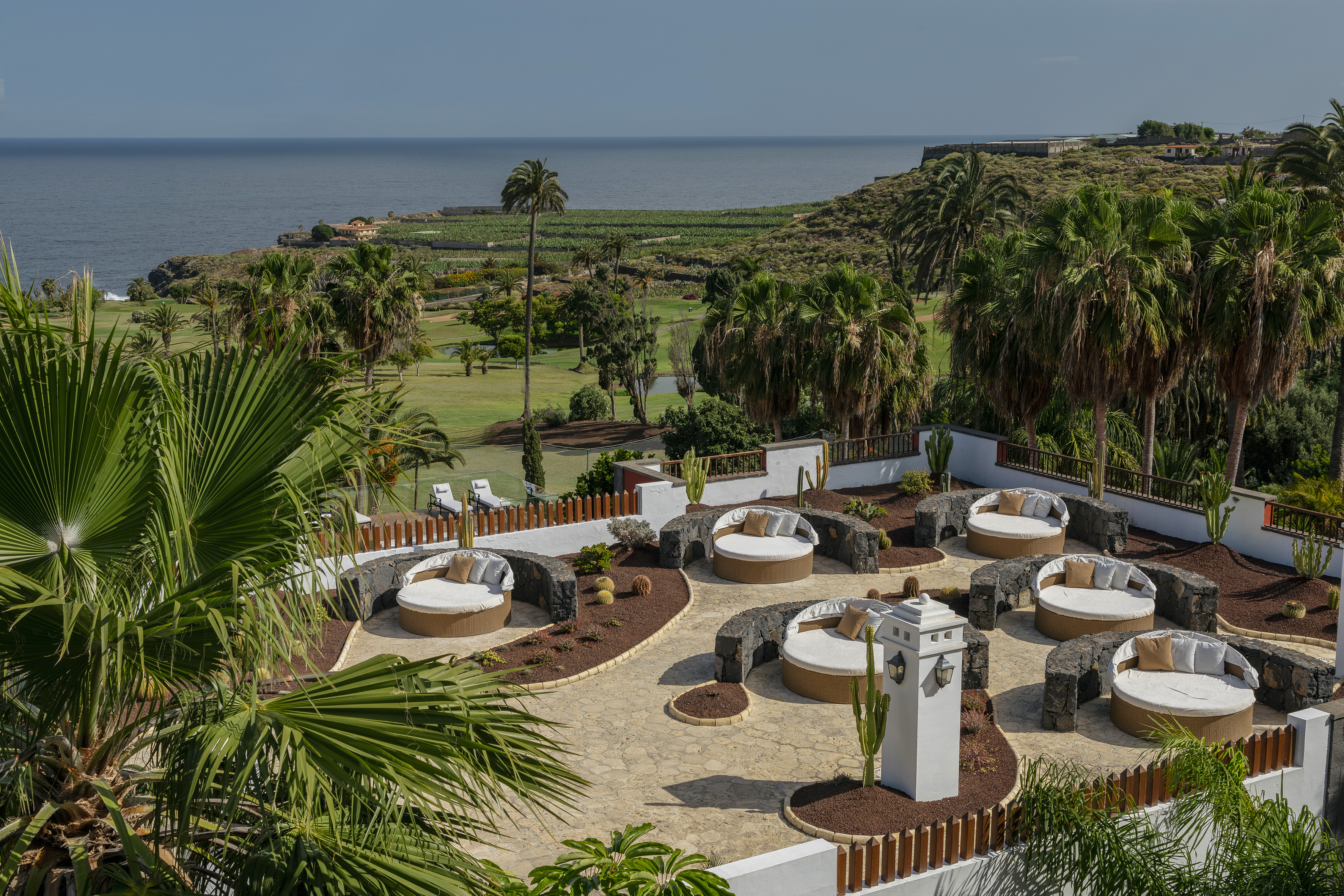Luxury resort patio with round daybeds overlooking golf course and ocean.