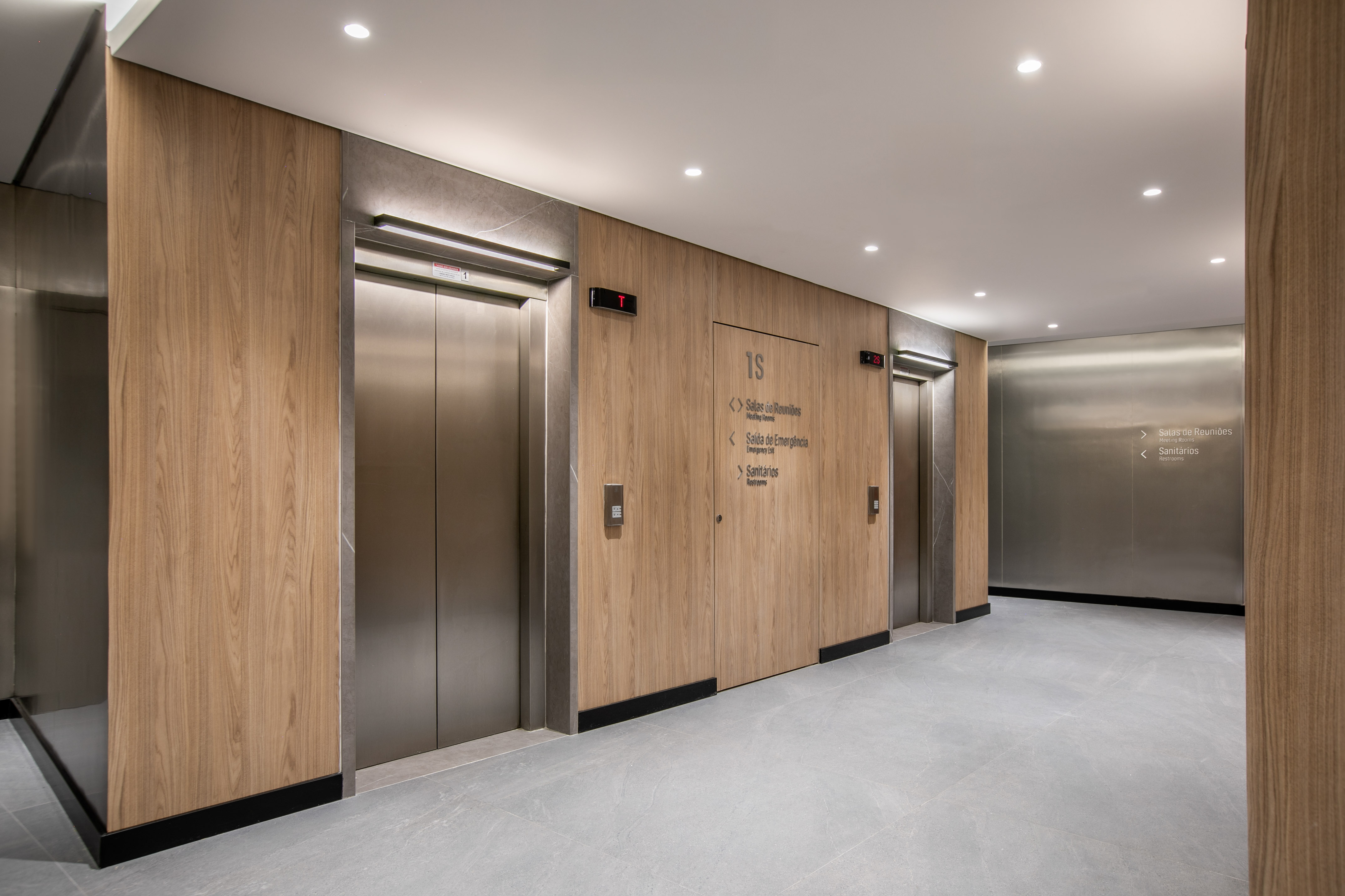 Modern lobby, wood panels, two stainless steel elevators, and directional signs.