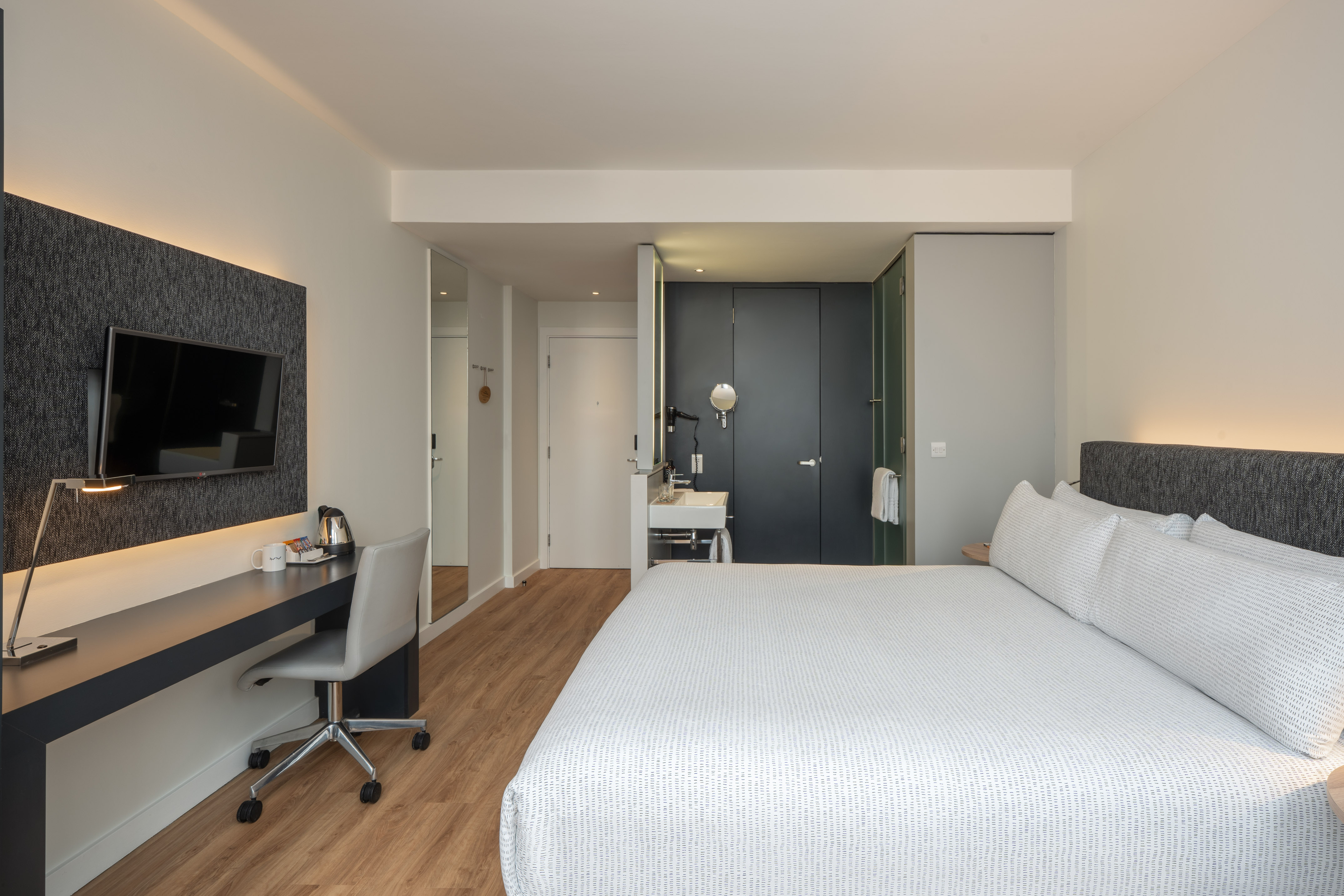 Modern hotel room with king bed, work desk, and integrated vanity.