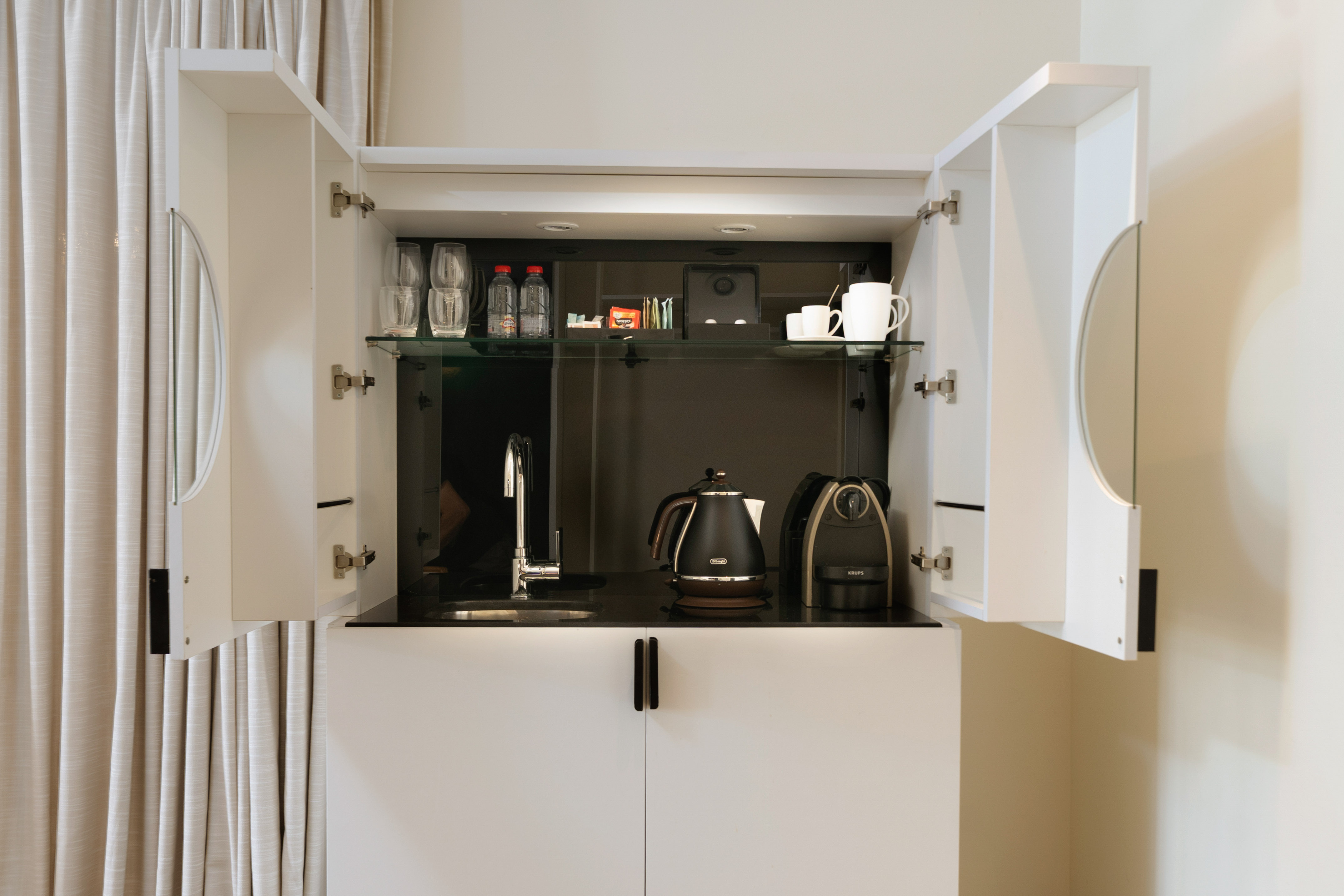 Modern hotel room kitchenette with coffee machine, kettle, and sink.