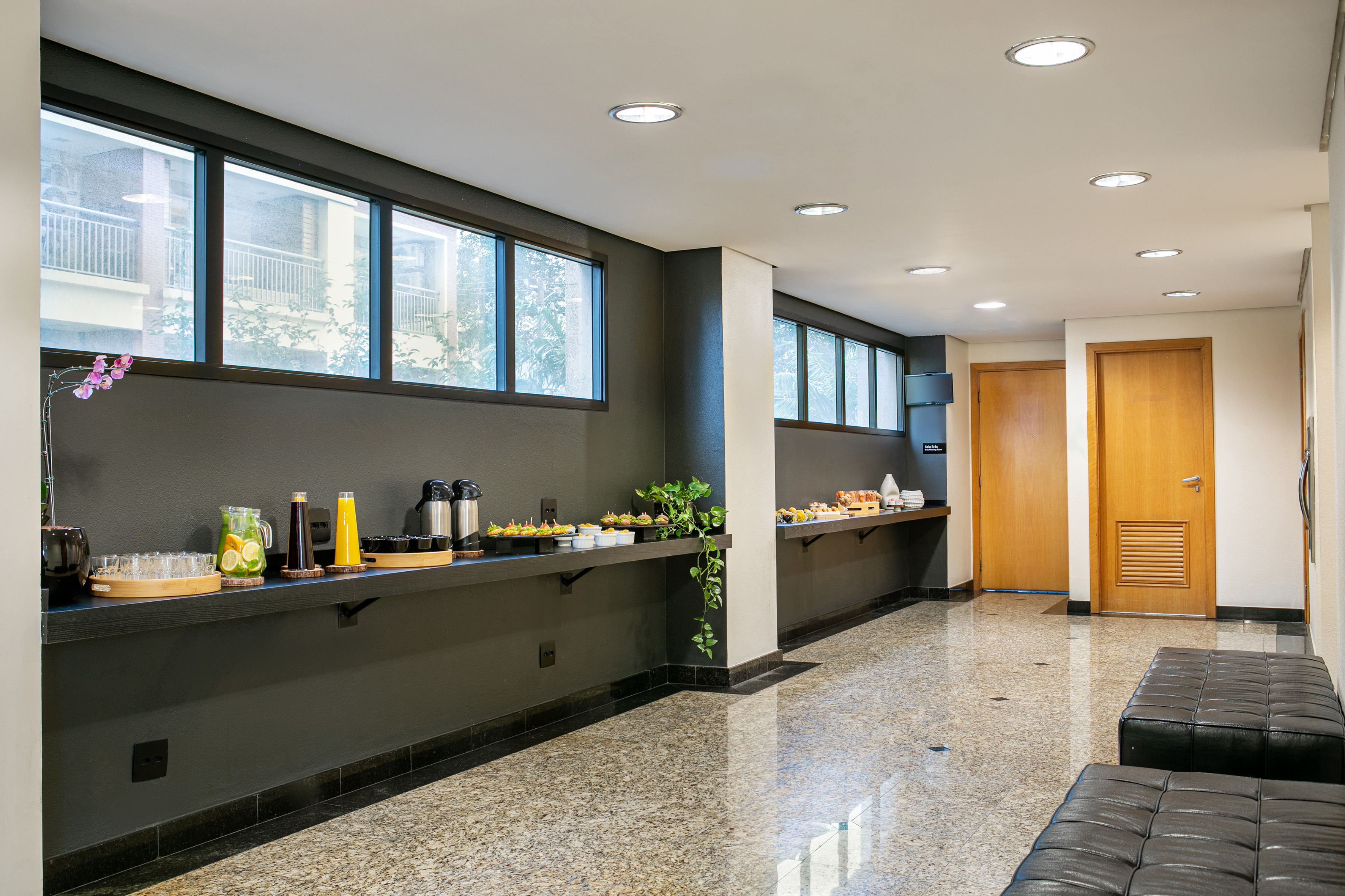 Modern hallway refreshment buffet with drinks, snacks, and black seating.