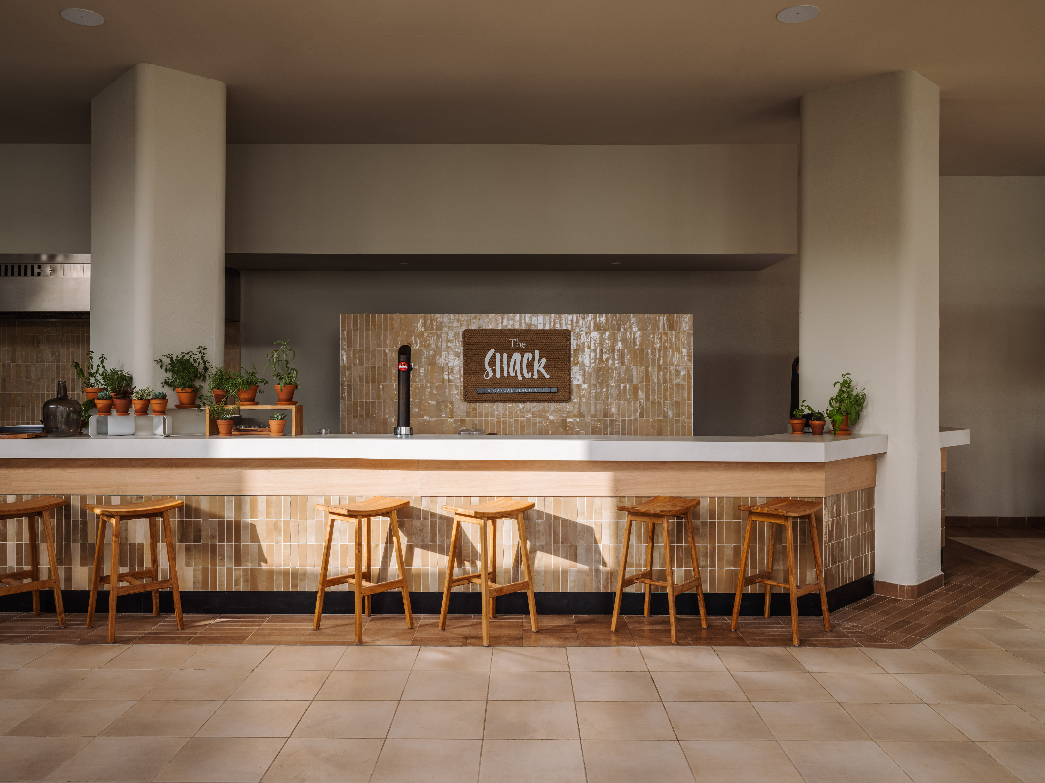 The Shack modern bar with wooden stools, tiled counter, and potted plants.