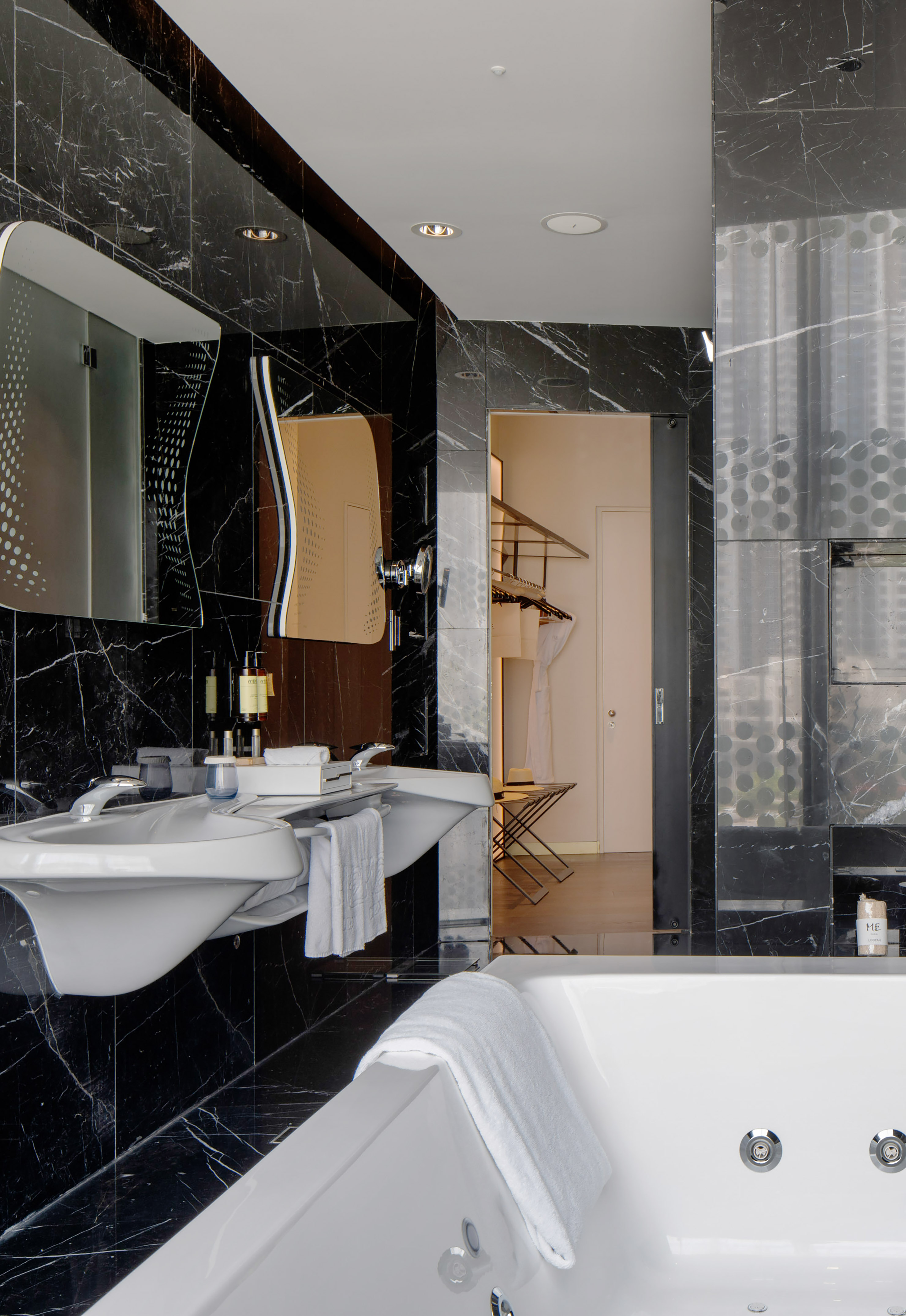 Black marble bathroom with double vanity, modern fixtures, and white tub.