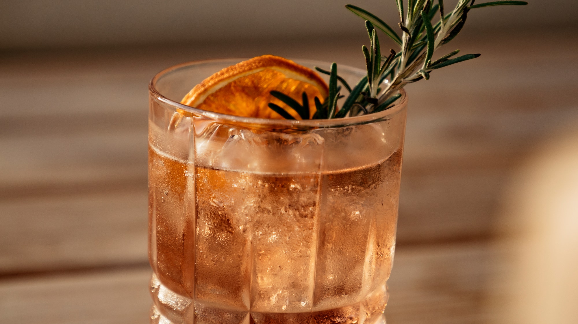 a glass of liquid with a slice of orange and rosemary