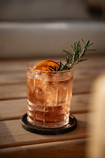 a glass of liquid with a slice of orange and rosemary