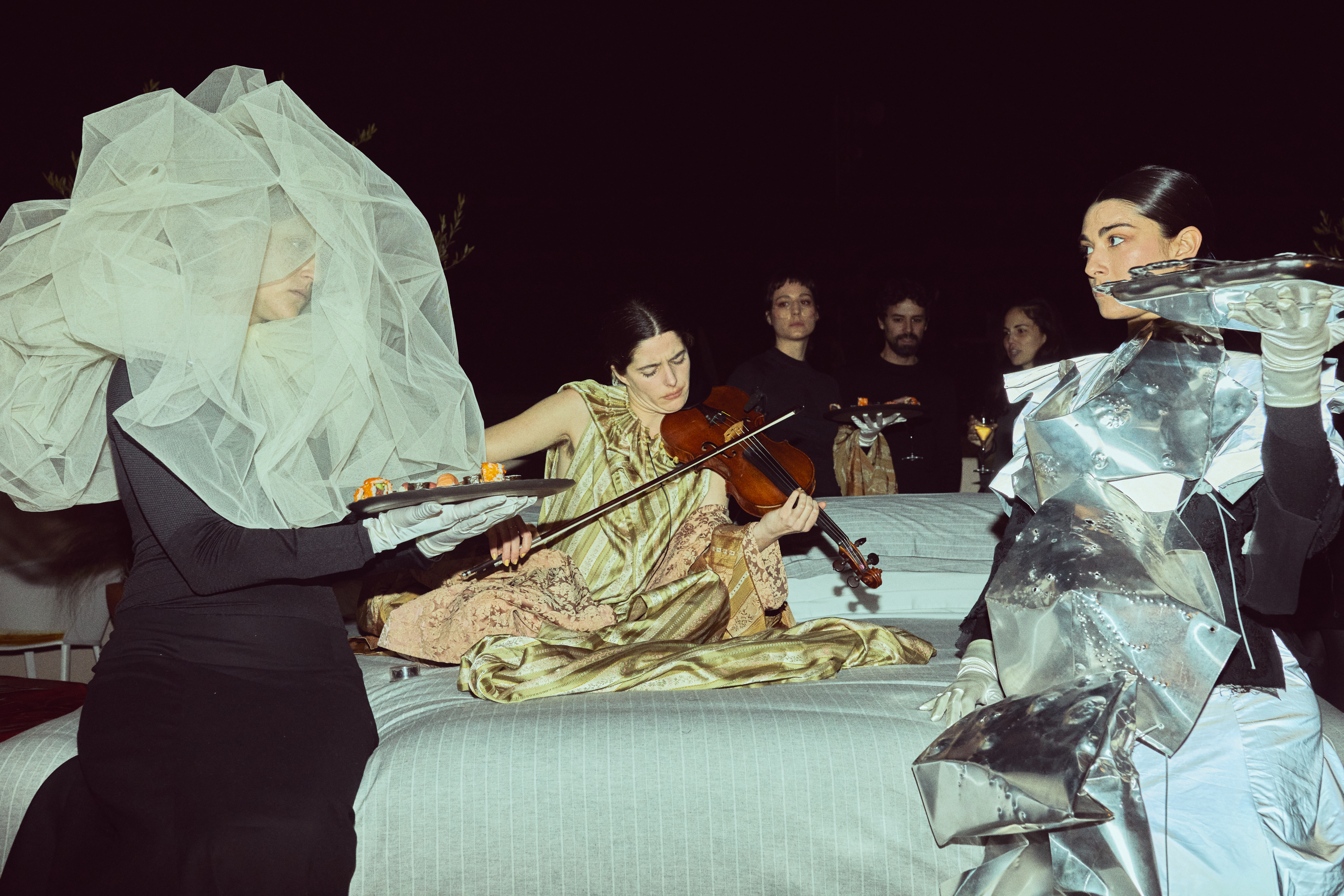 Performance art: Violinist, tulle-covered server with sushi, and metallic-clad figure.