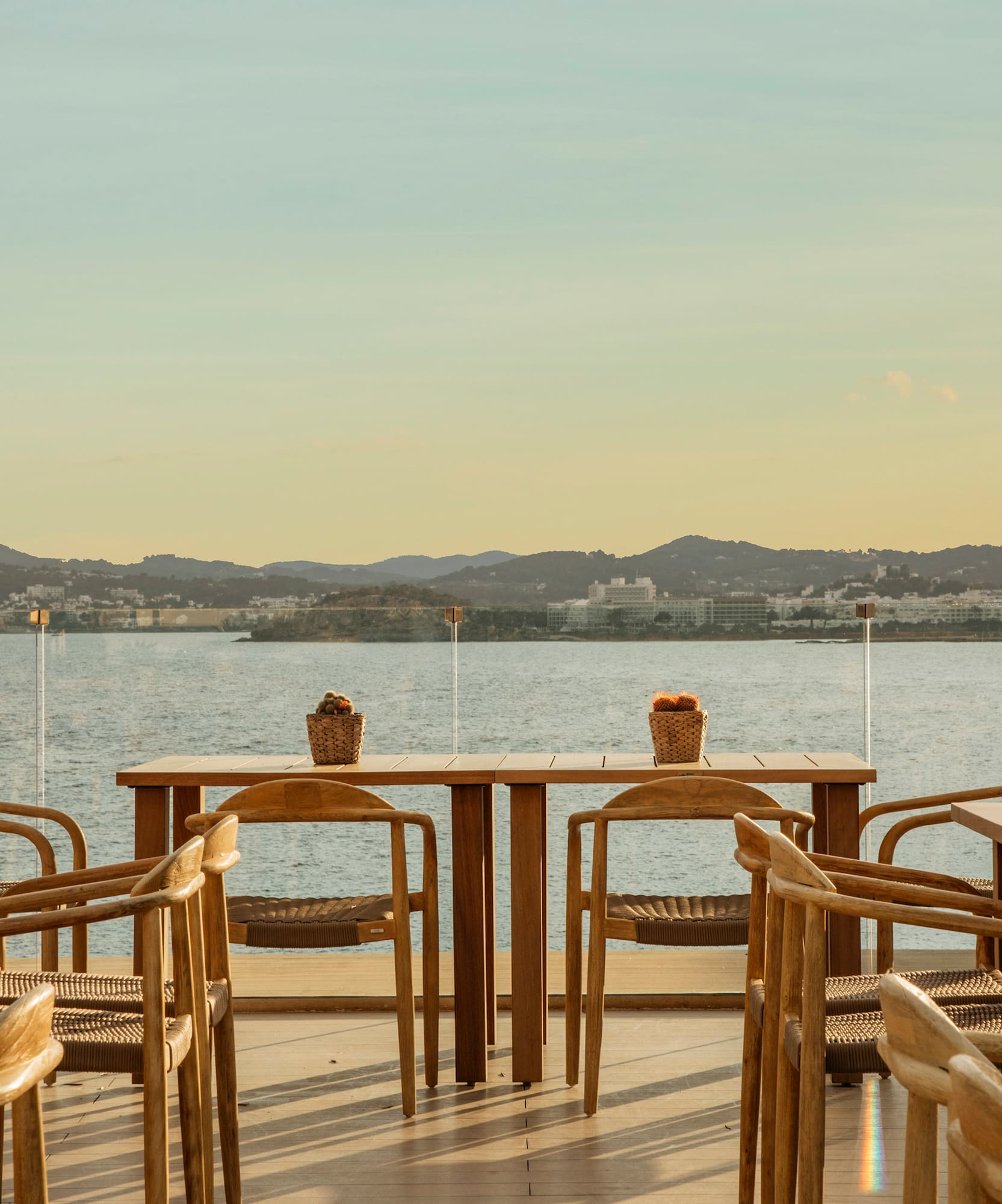 Coastal outdoor restaurant terrace with wooden tables, sea view, and sunset.