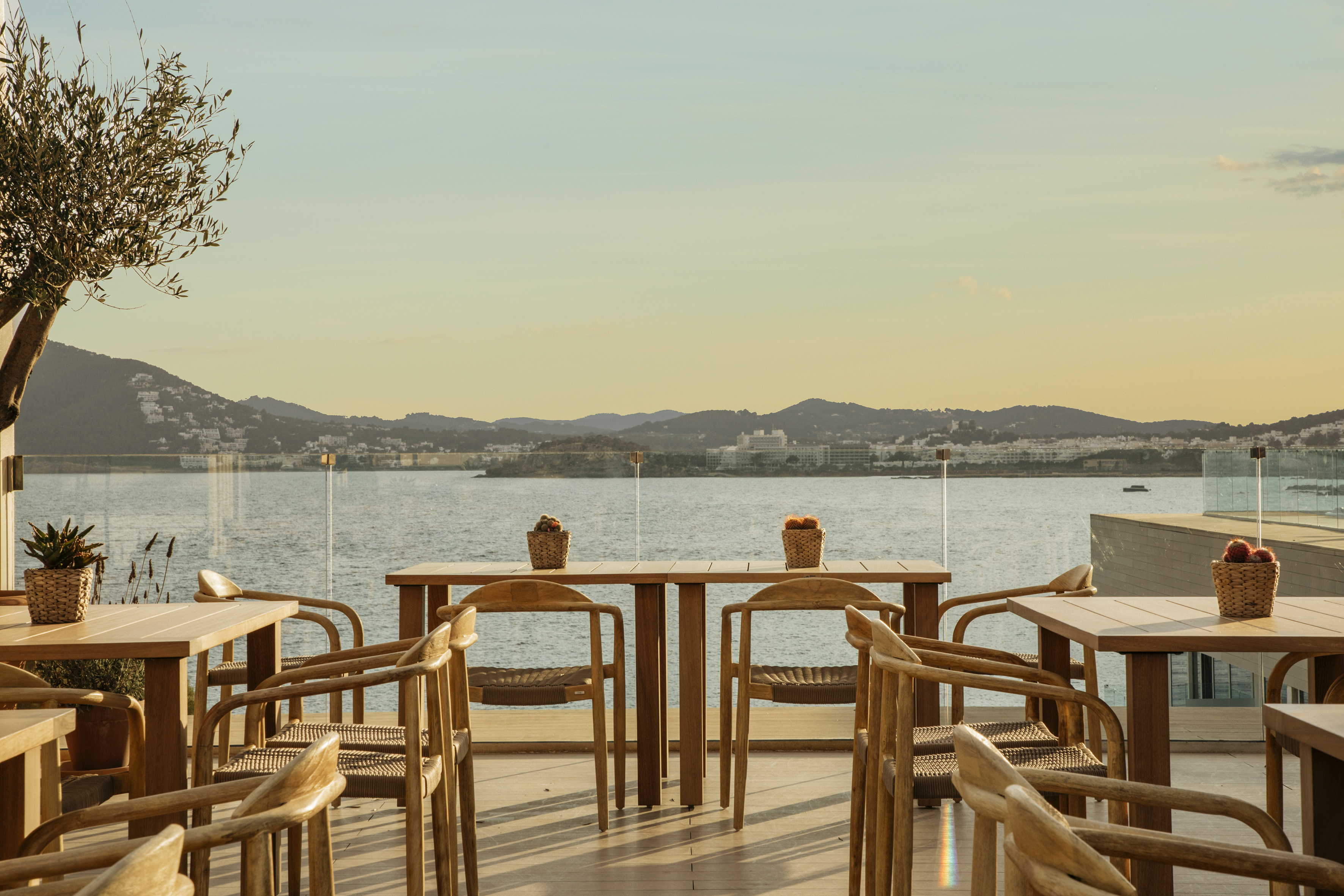 Coastal outdoor restaurant terrace with wooden tables, sea view, and sunset.