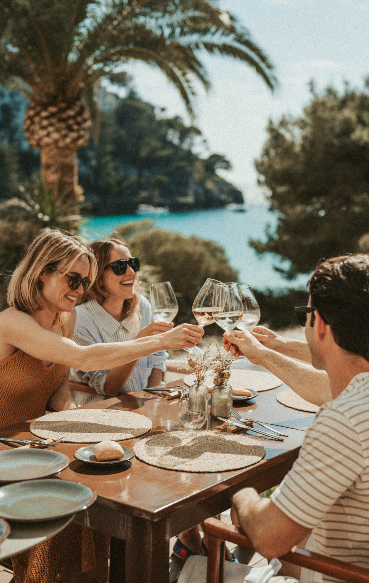 Friends toasting wine glasses at coastal outdoor dining table with ocean view.